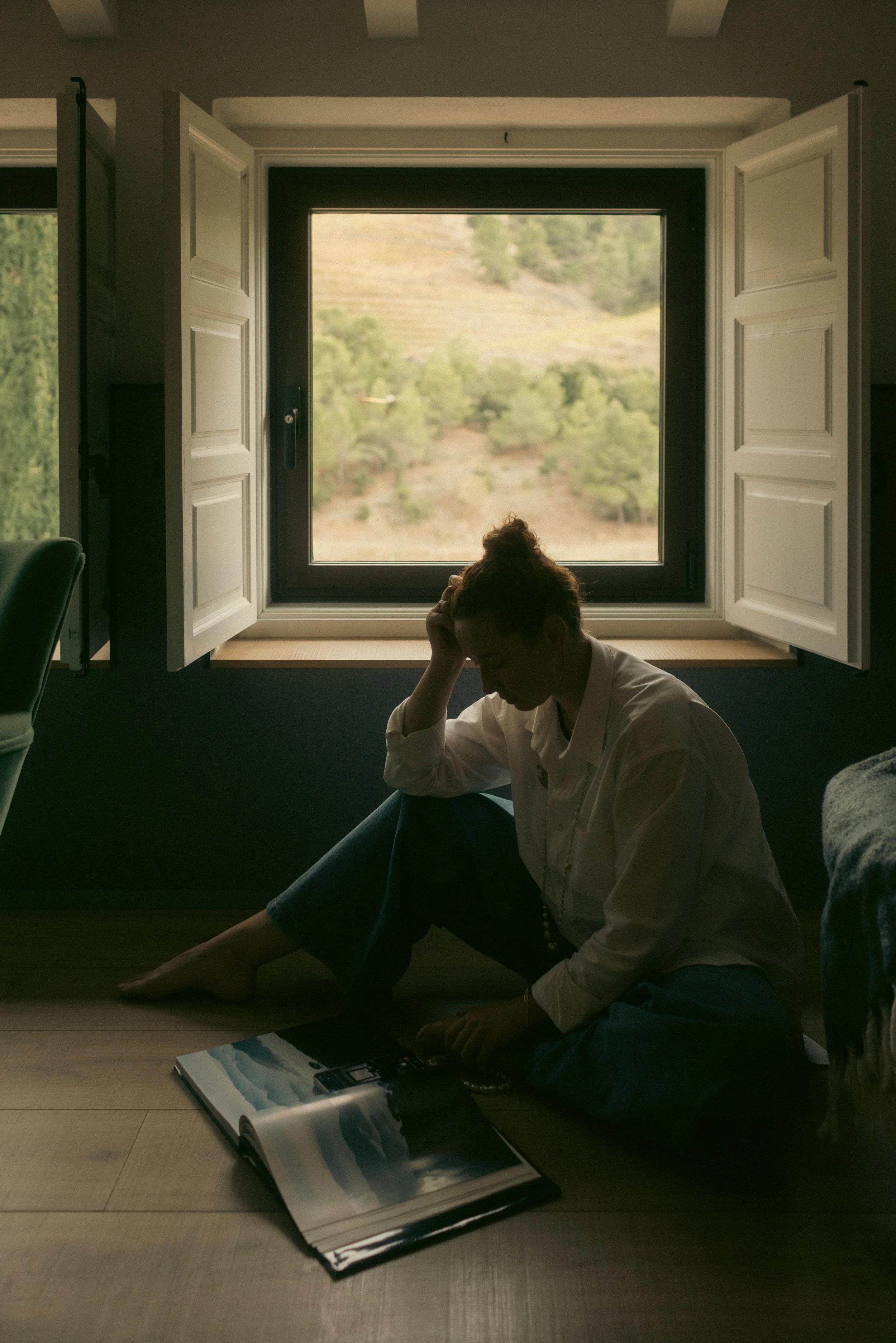 Quiet contemplation at Terra Dominicata: guest engrossed in a detailed book about Priorat wine by an open window overlooking the vineyard hills.