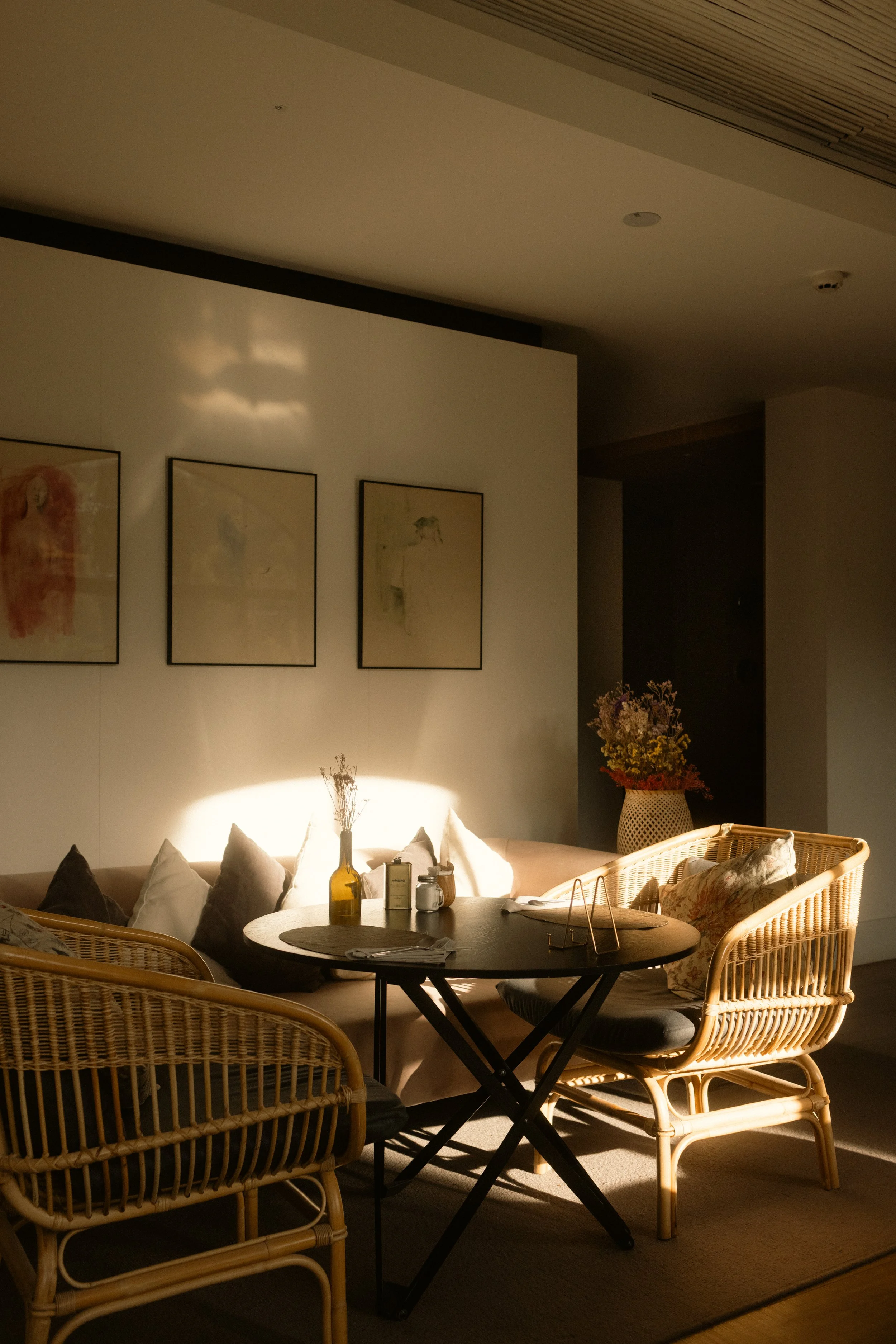 Terra Dominicata luxury boutique hotel in Priorat. Cozy interior corner with rattan chairs, a round table, and curated framed artwork in warm natural sunlight. Professional hospitality photography by Valerie.