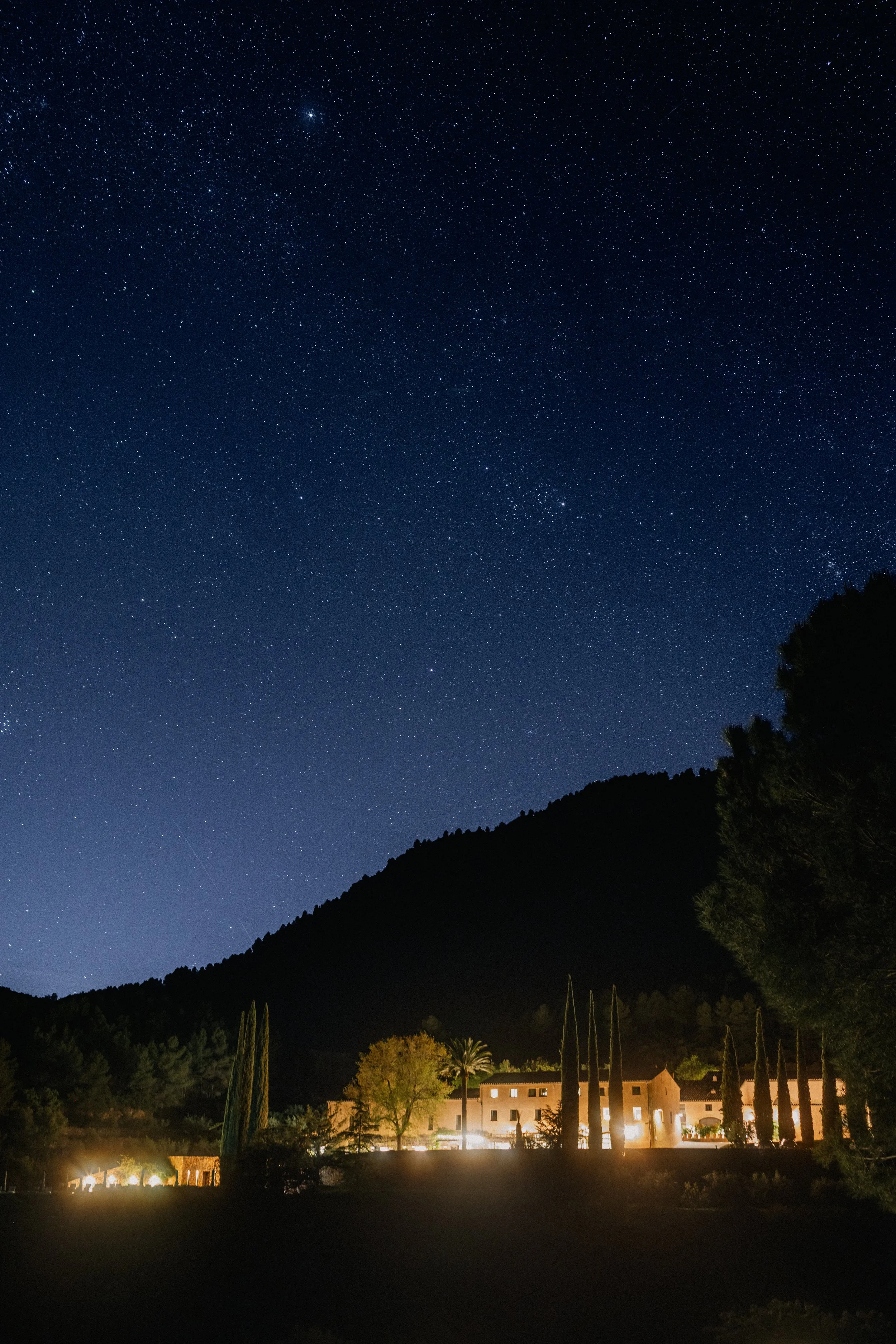 Terra Dominicata hotel and destination photography, starry night sky over the surrounding mountains with the hotel illuminated below, Priorat, Catalonia, Spain.
