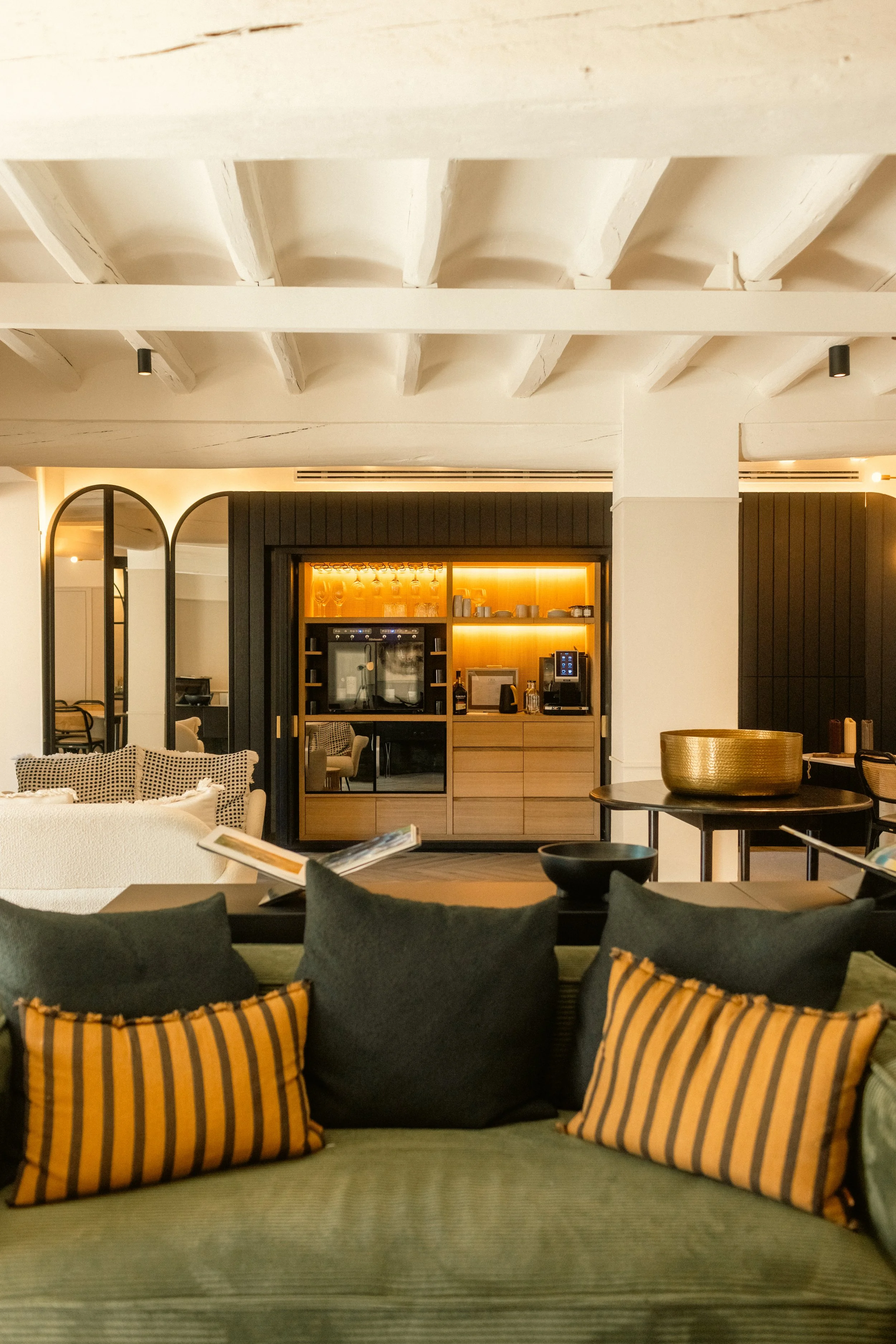 Luxury hotel interior photography: cozy lounge area with green velvet sofa, wood-paneled bar, and warm accent lighting. Professional architectural and hospitality portfolio shot at Ora Priorat.