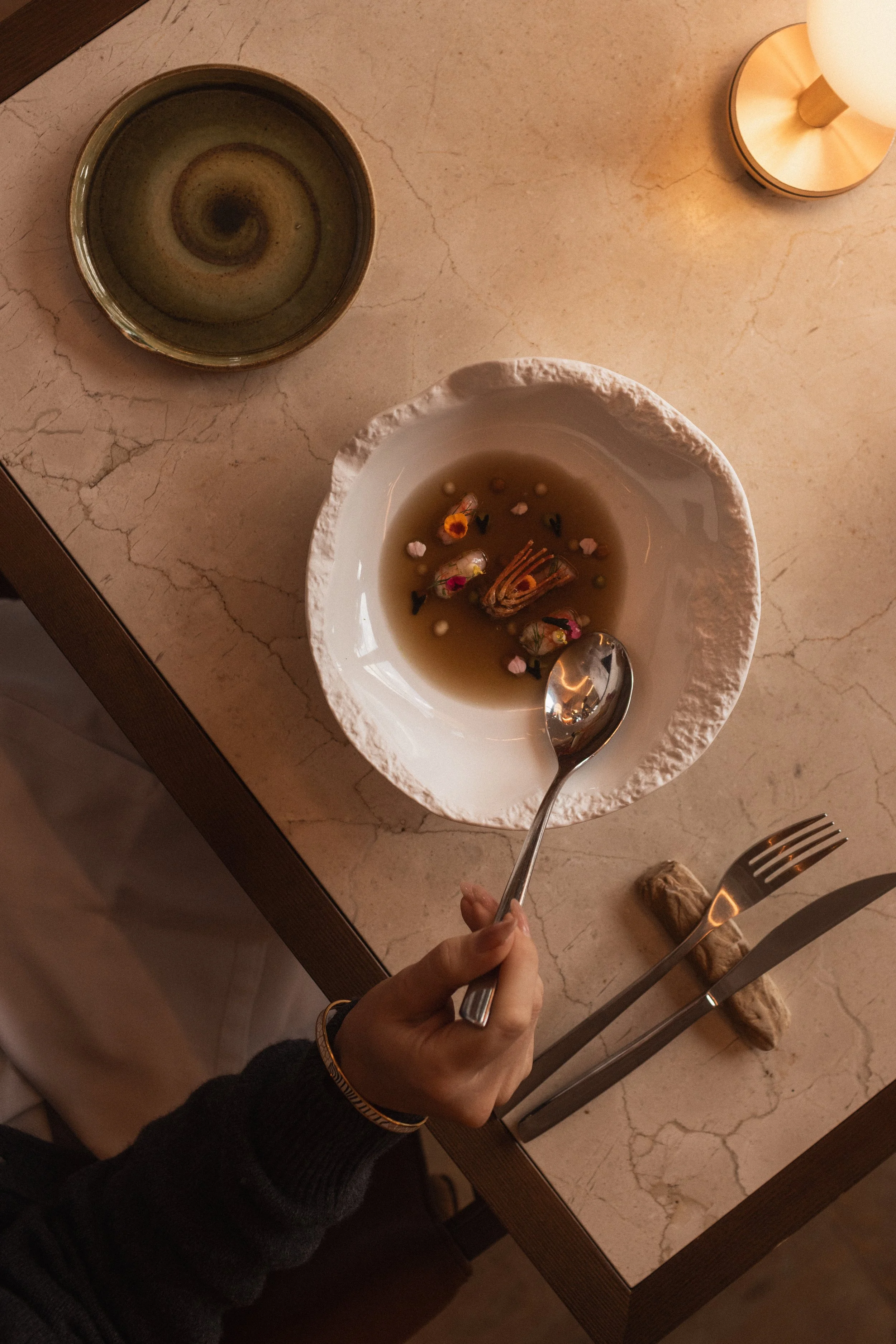 Mas d'en Bruno luxury hotel fine dining photography. Gourmet seafood soup with edible flowers on a marble table at the restaurant. Professional gastronomy imagery by Valerie.