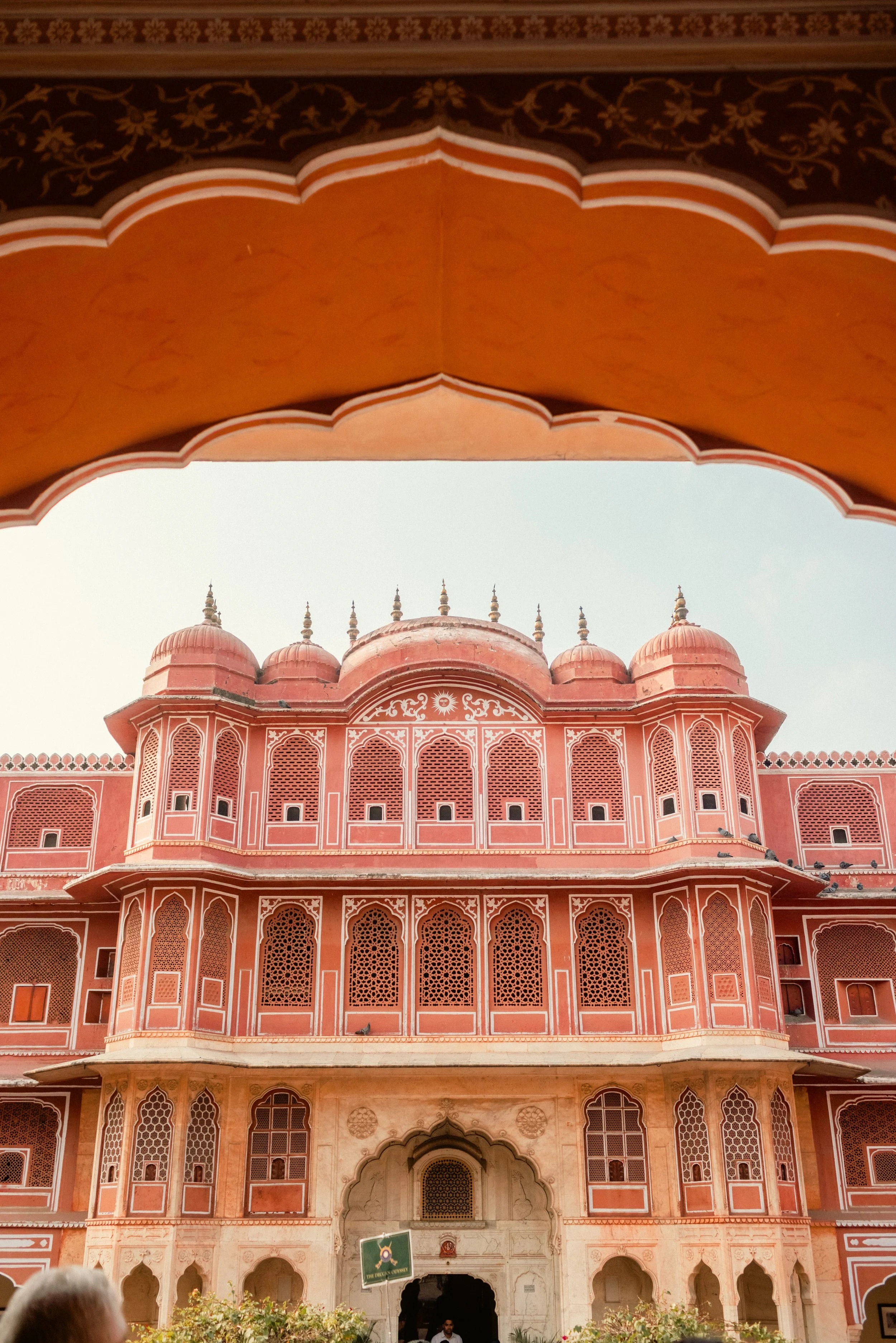 Architectural hospitality photography: Ornate pink historic building framed by a stone archway. Professional travel and heritage site imagery for Deccan Odyssey.