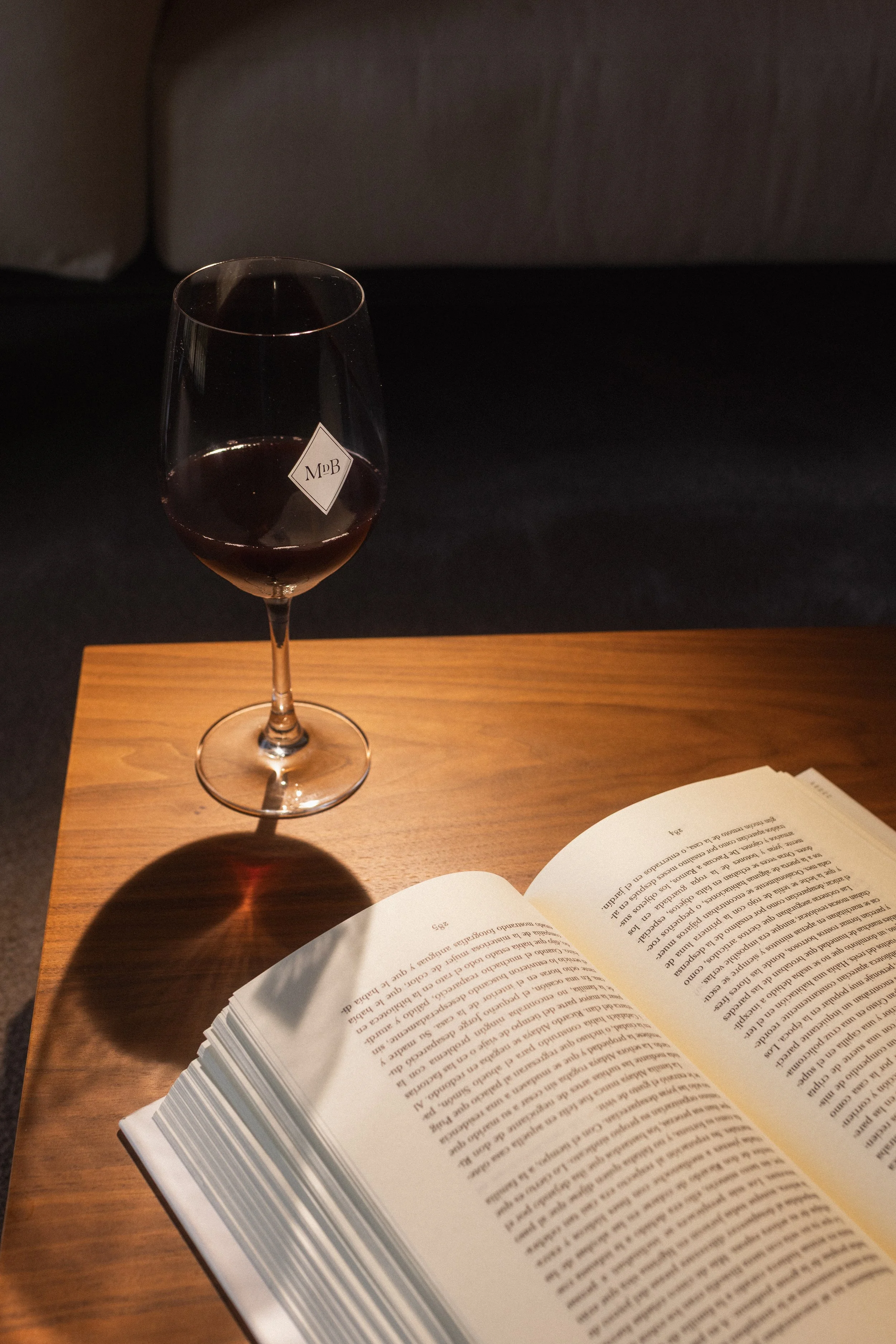 Relaxed sophistication at Mas d'en Bruno: a glass of deep Priorat red wine and an open book on a wooden table, capturing the essence of a quiet retreat.