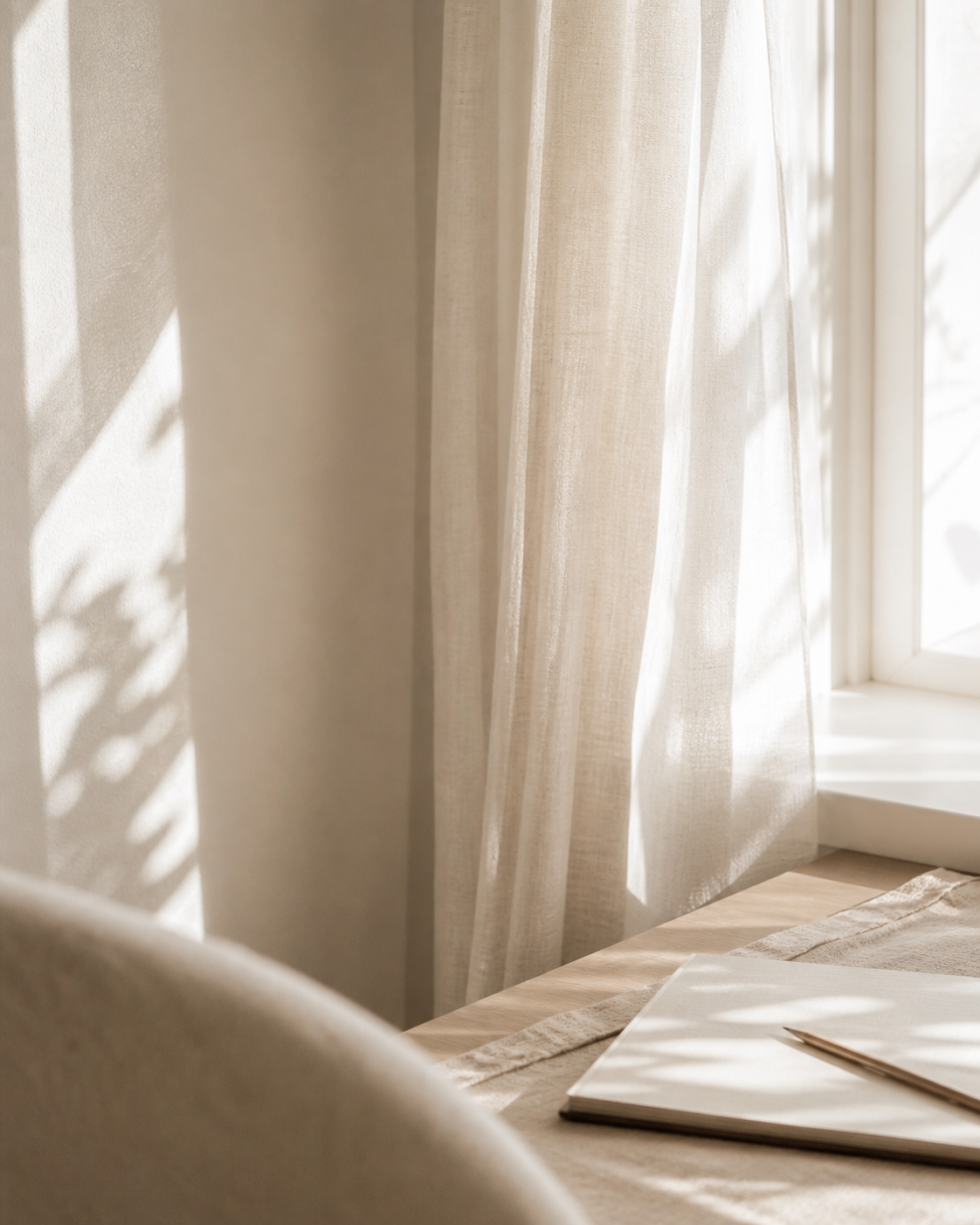 Sonnenlicht fällt durch einen weißen Vorhang und wirft Schatten an die Wand neben einem Fenster.