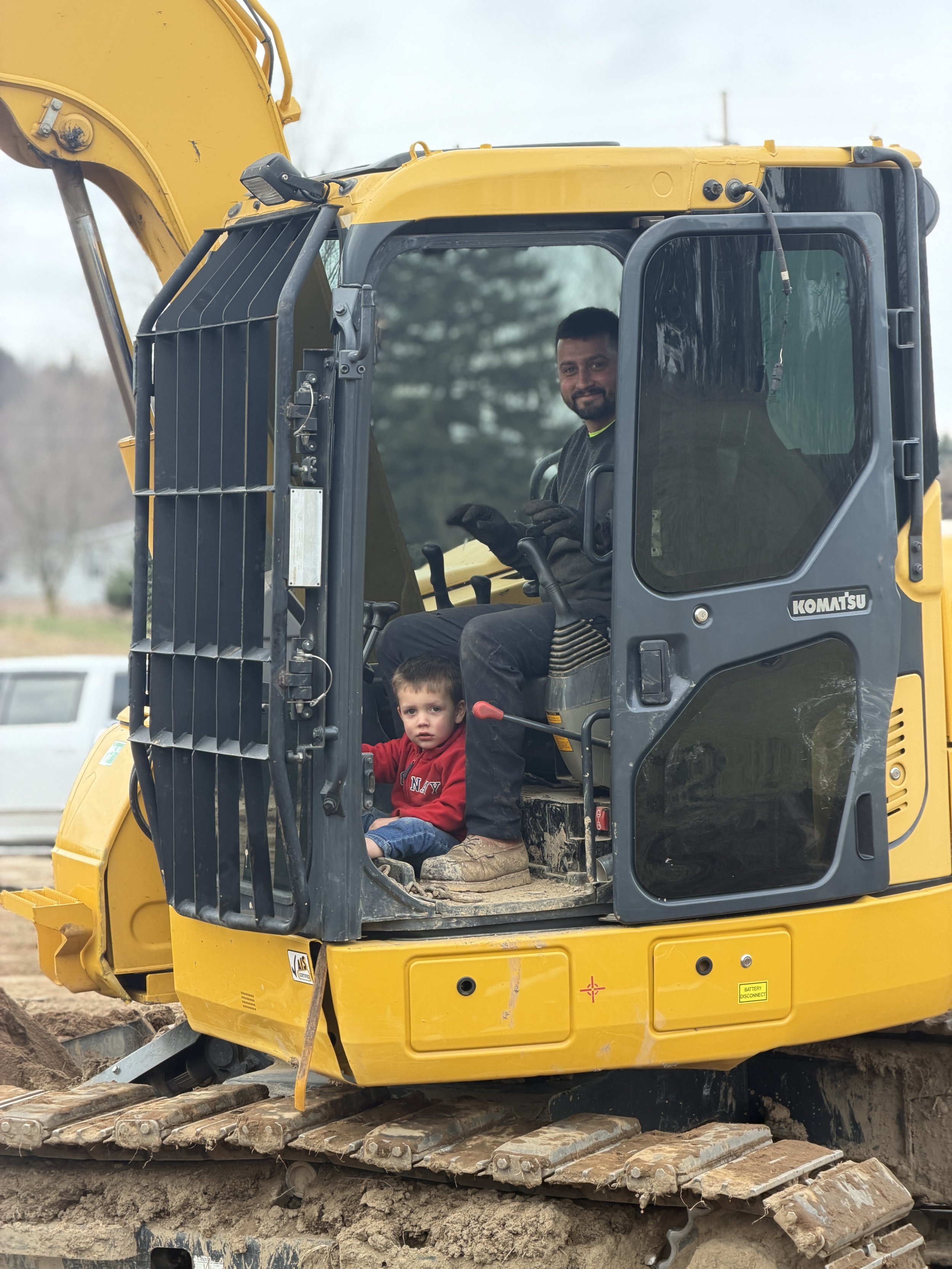 Man and young boy sitting inside the cab of a yellow construction excavator.