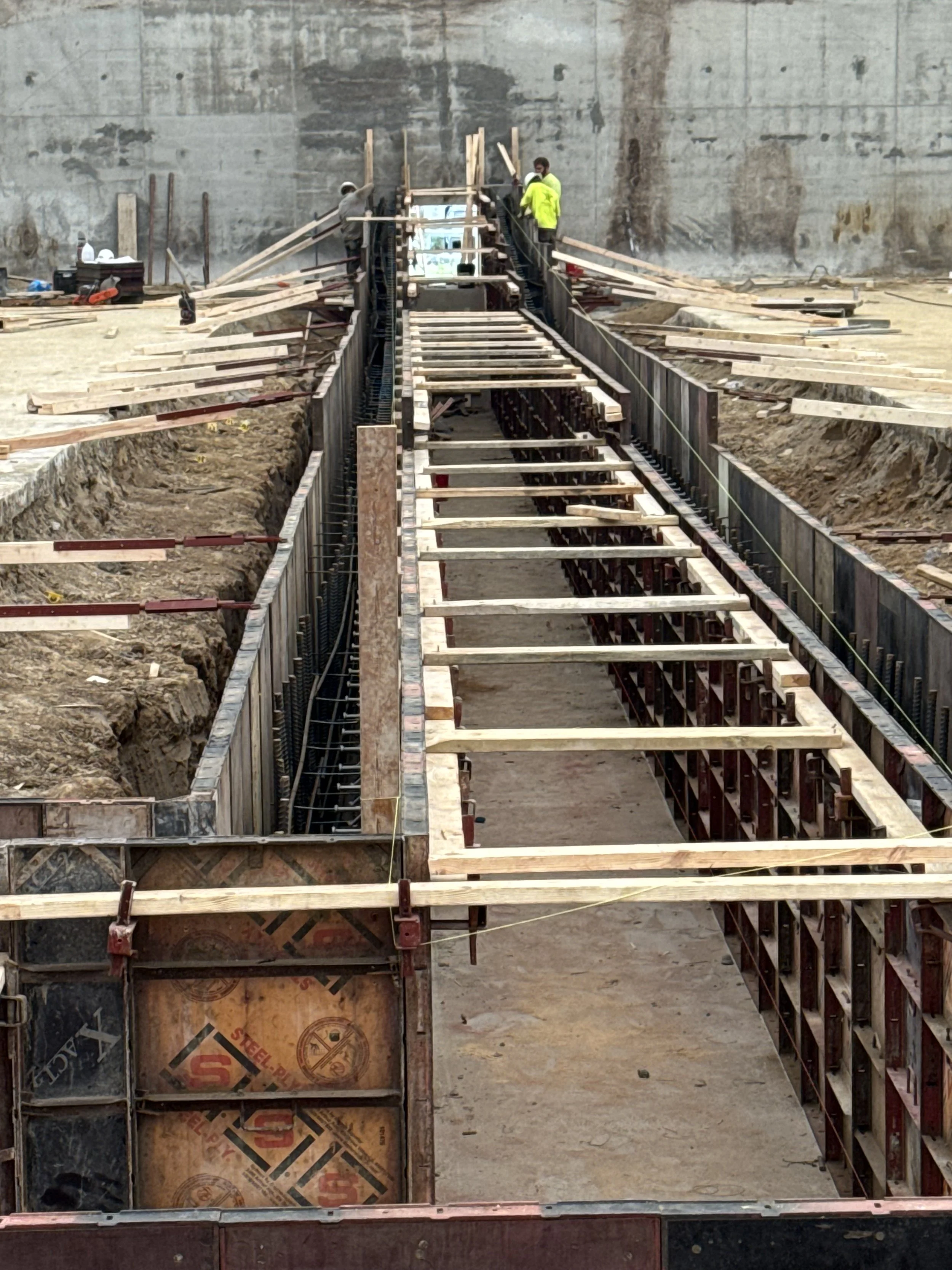 Construction workers assembling steel rebar and wooden formwork for a concrete structure in an indoor construction site.