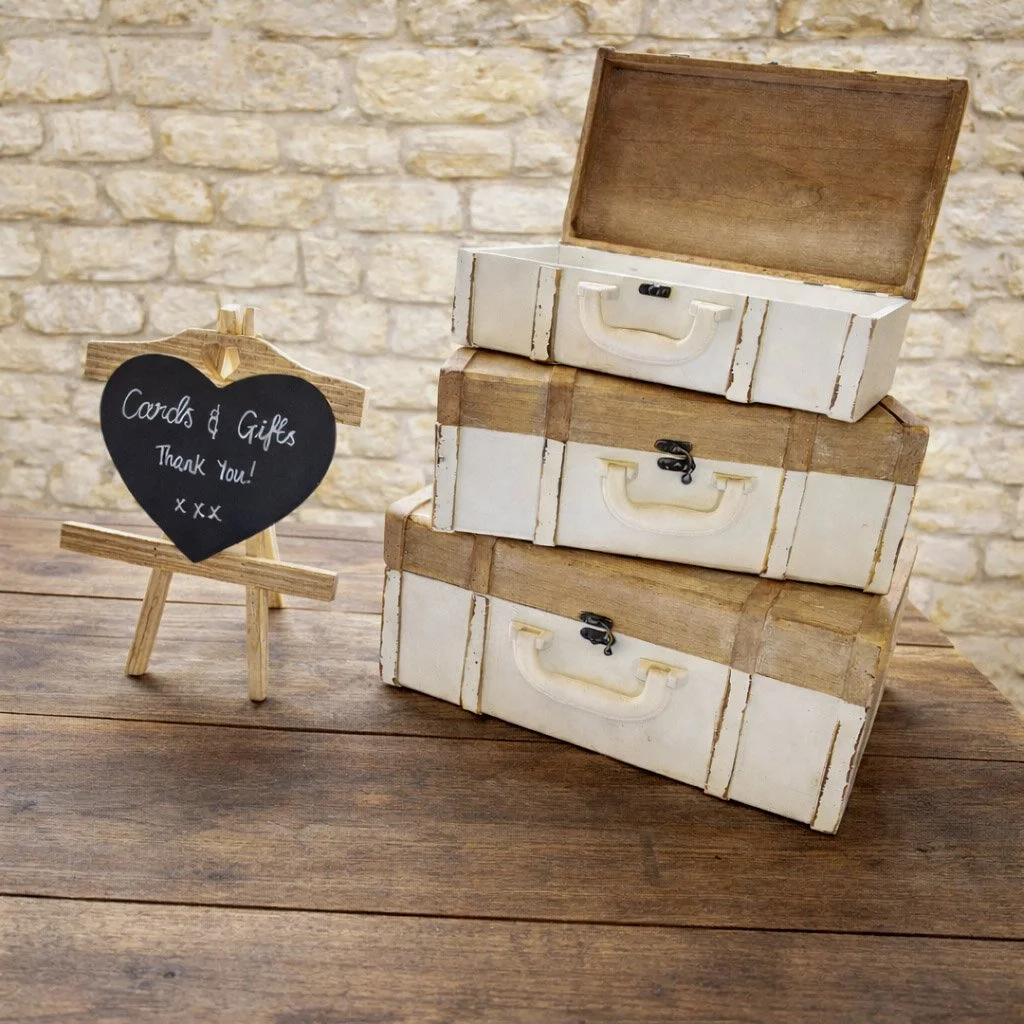 Stacked vintage suitcases with a small chalkboard sign on a wooden table. The sign reads 'Cards & Gifts, Thank you! xxx'.