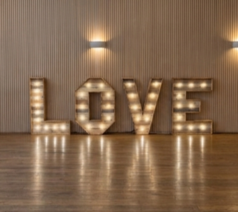 Large illuminated sign spelling 'LOVE' on a wooden floor with a textured wall background.
