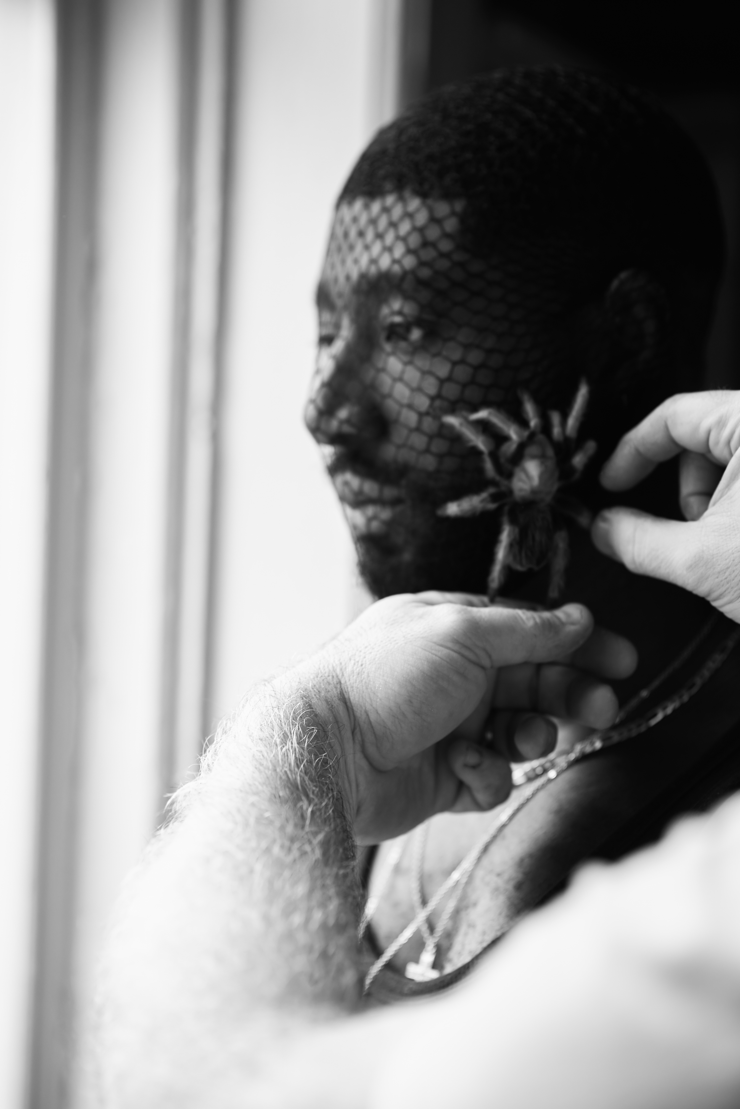 A person with a fishnet mask over their face is being adjusted or placed by another person's gloved hands.