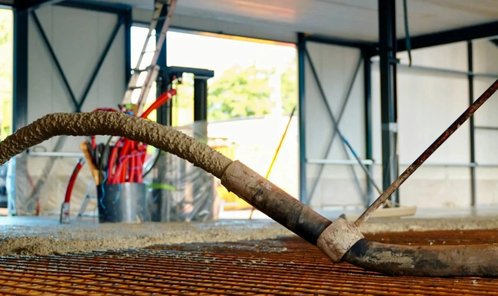 Een betonstort met een slang op een bouwplaats, met wapening en een bouwconstructie op de achtergrond.