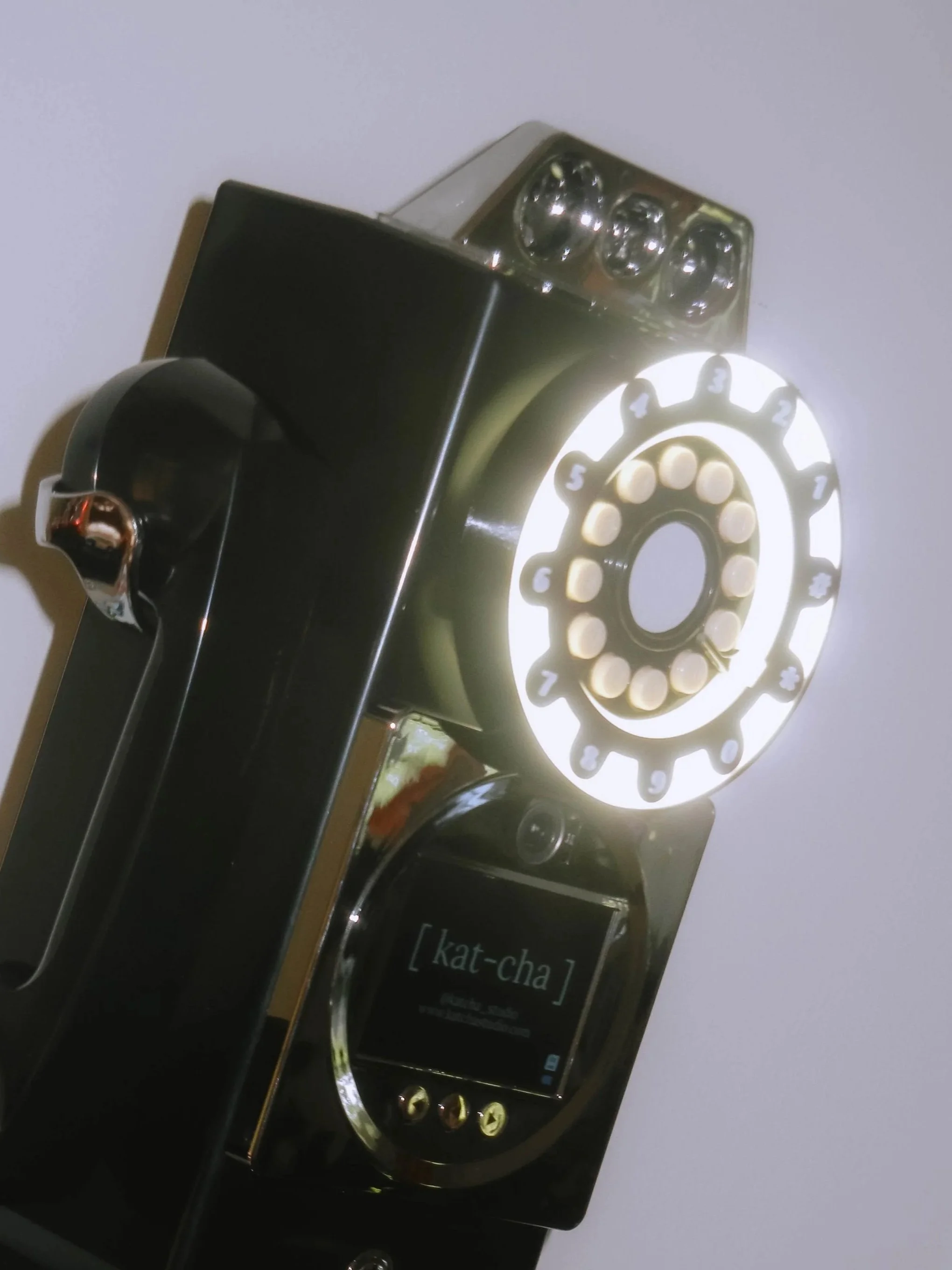 Close-up of a modern smartphone with an illuminated rotary dial pad displaying numbers 1 to 9. The phone is placed on a flat surface with a plain light background.