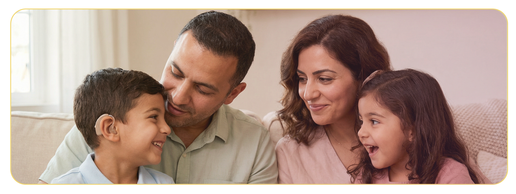 A happy family of four sitting closely on a beige couch in a living room. The father and son are smiling and looking at each other, while the mother and daughter are also smiling and looking at each other. The scene is warm and cheerful.