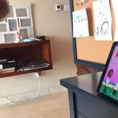 A computer monitor displays cartoon characters in a room with colorful children's drawings on a corkboard.