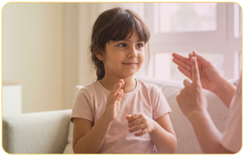 A young girl gives a high five to an adult in a light-colored room with a window in the background.