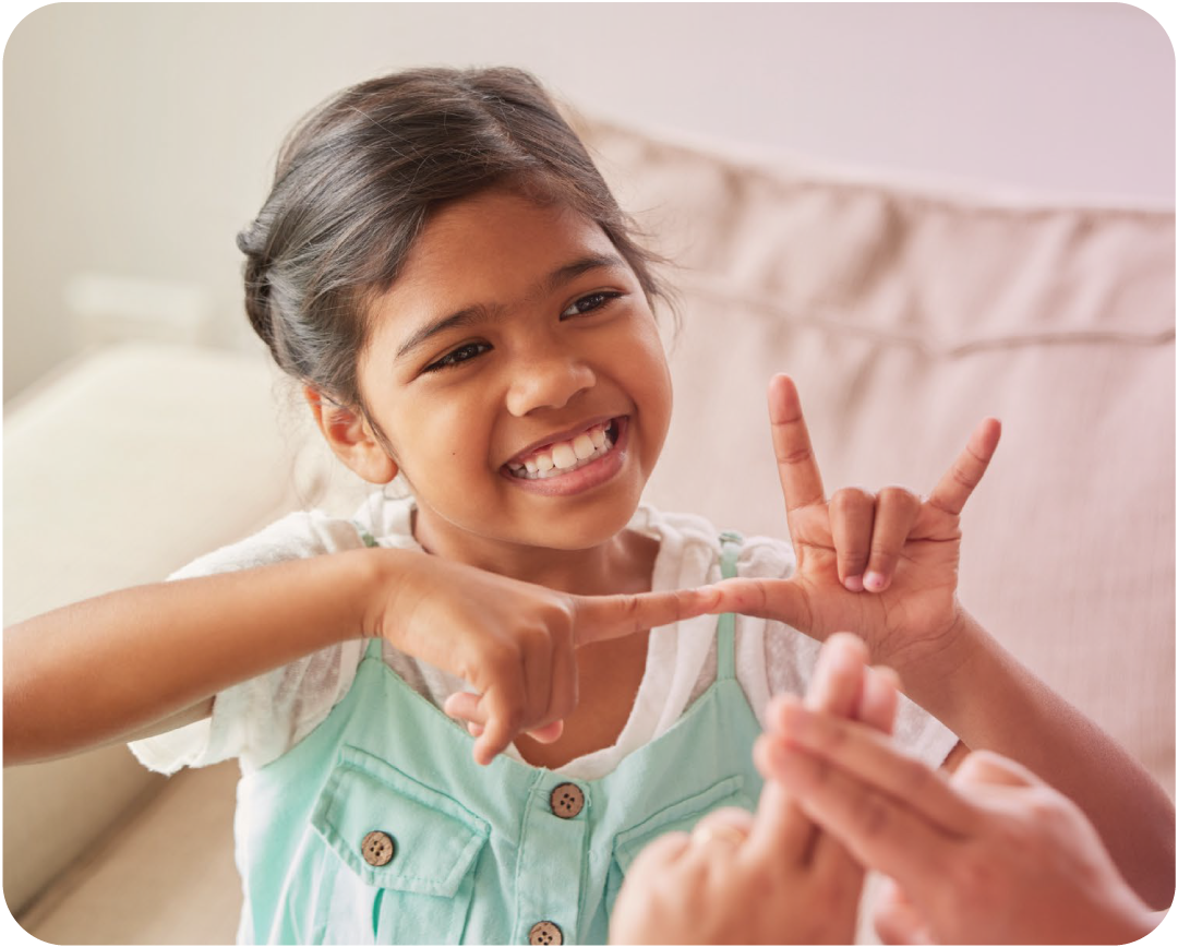 Young girl smiling and making a hand gesture with her fingers, sitting on a couch.