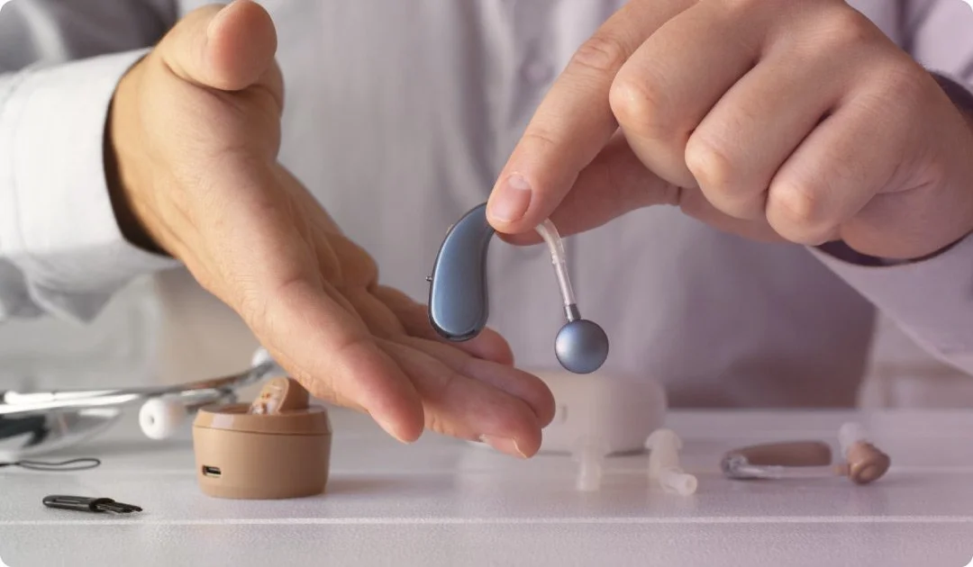 A person handling a hearing aid device over a table with other hearing aid parts and accessories.