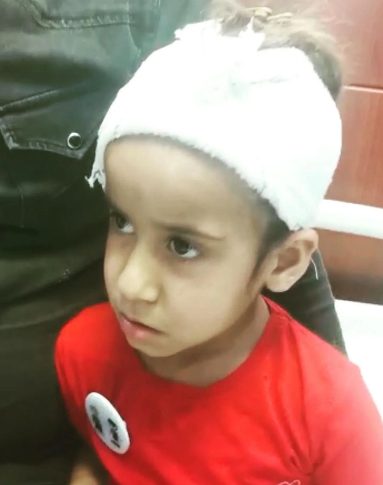 A young boy with a white headband and wearing a red shirt is looking slightly to the side.