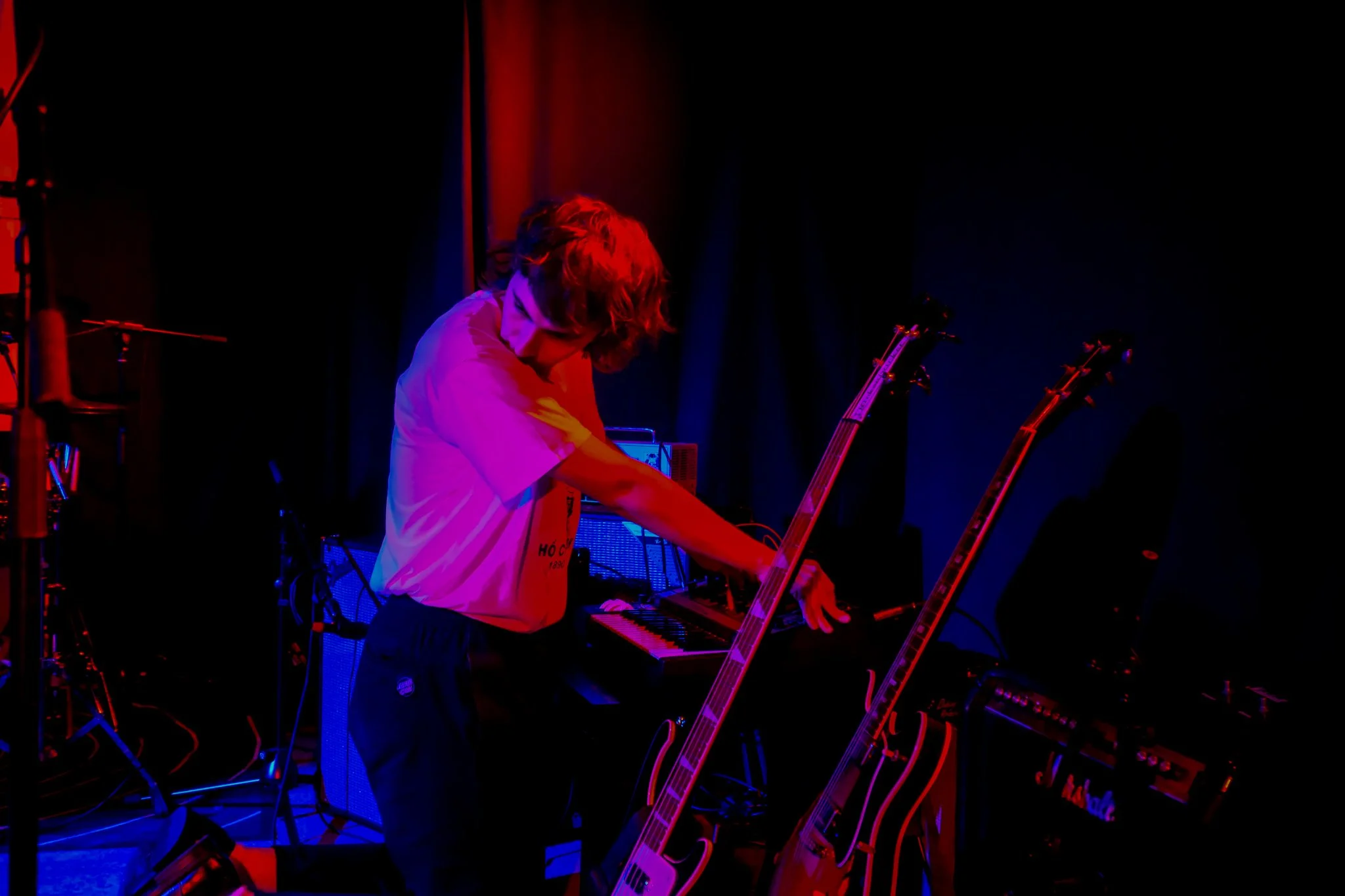 A person with red hair playing a keyboard on stage, surrounded by musical equipment, under colorful stage lighting.