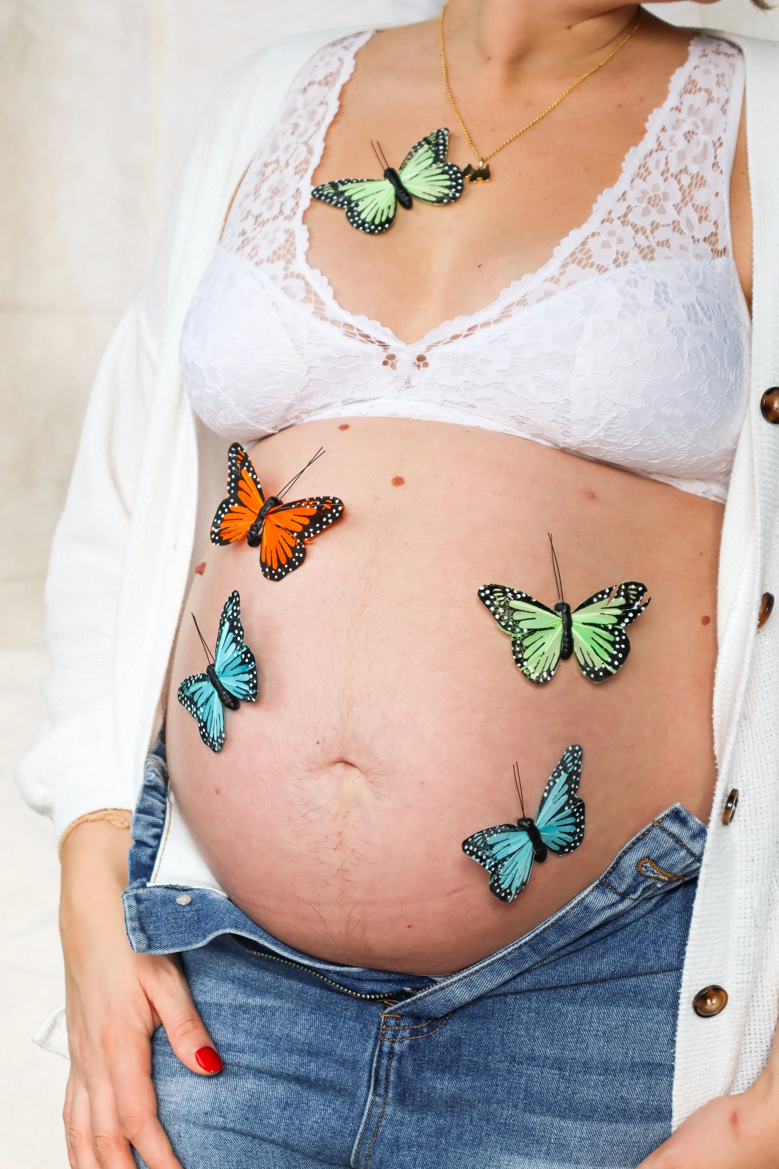A woman wearing a white lace bra, a white cardigan, and blue jeans with butterflies attached to her skin and clothing.