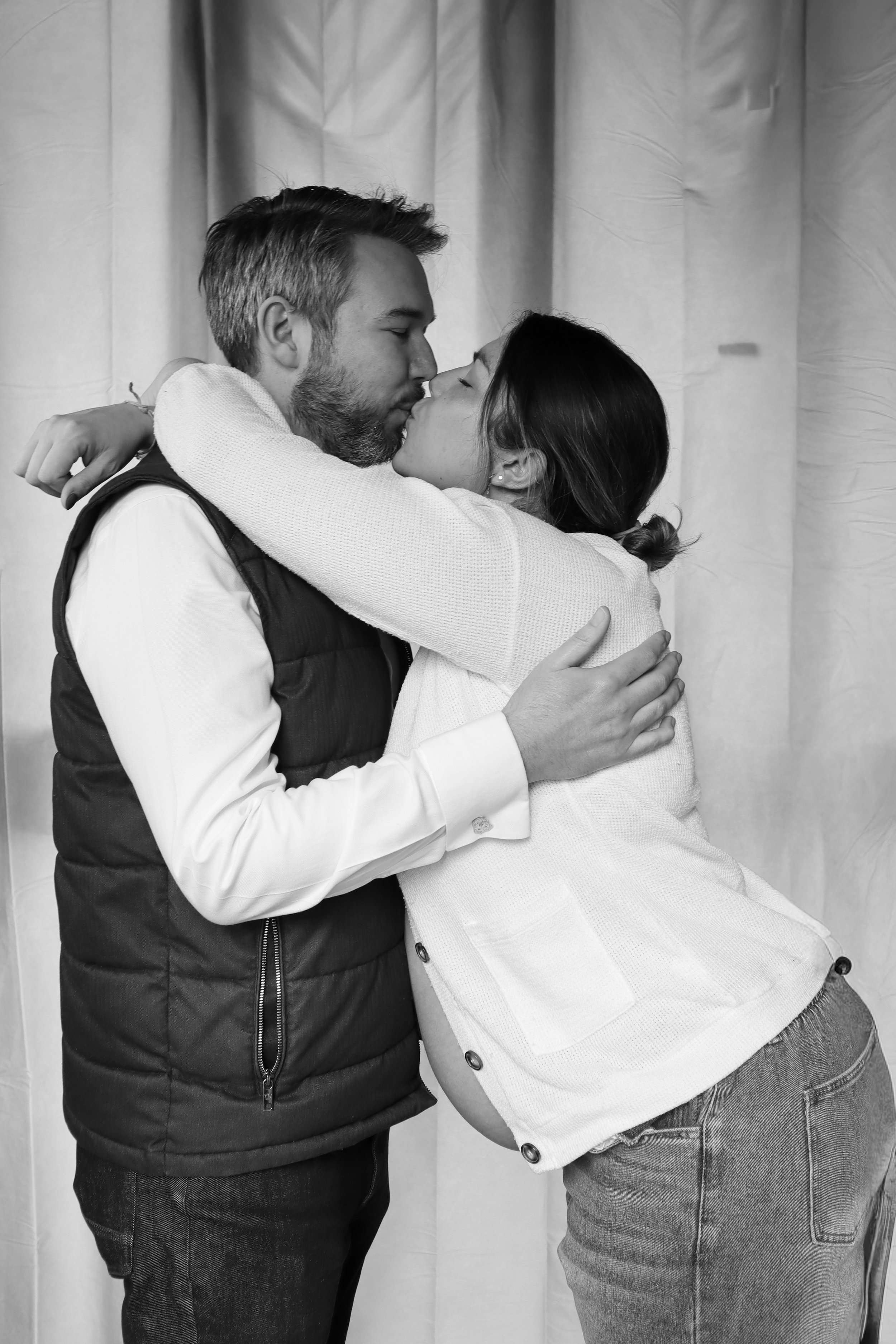 Black and white photo of a man and woman embracing and leaning in for a kiss, with a curtain background.
