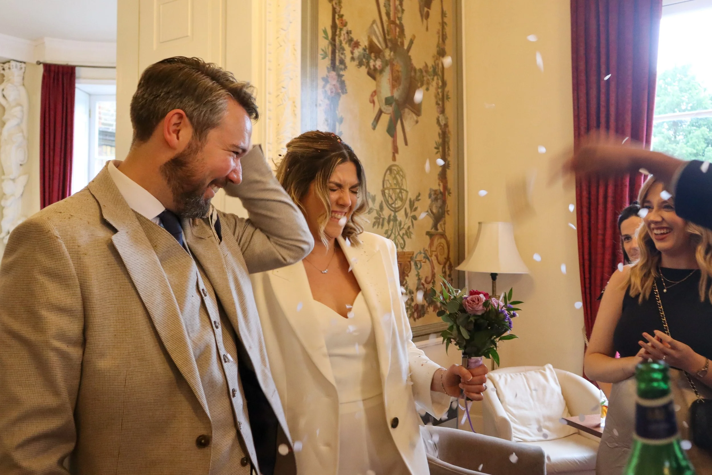 A man and woman smiling during a celebration, with a woman holding a bouquet of flowers.
