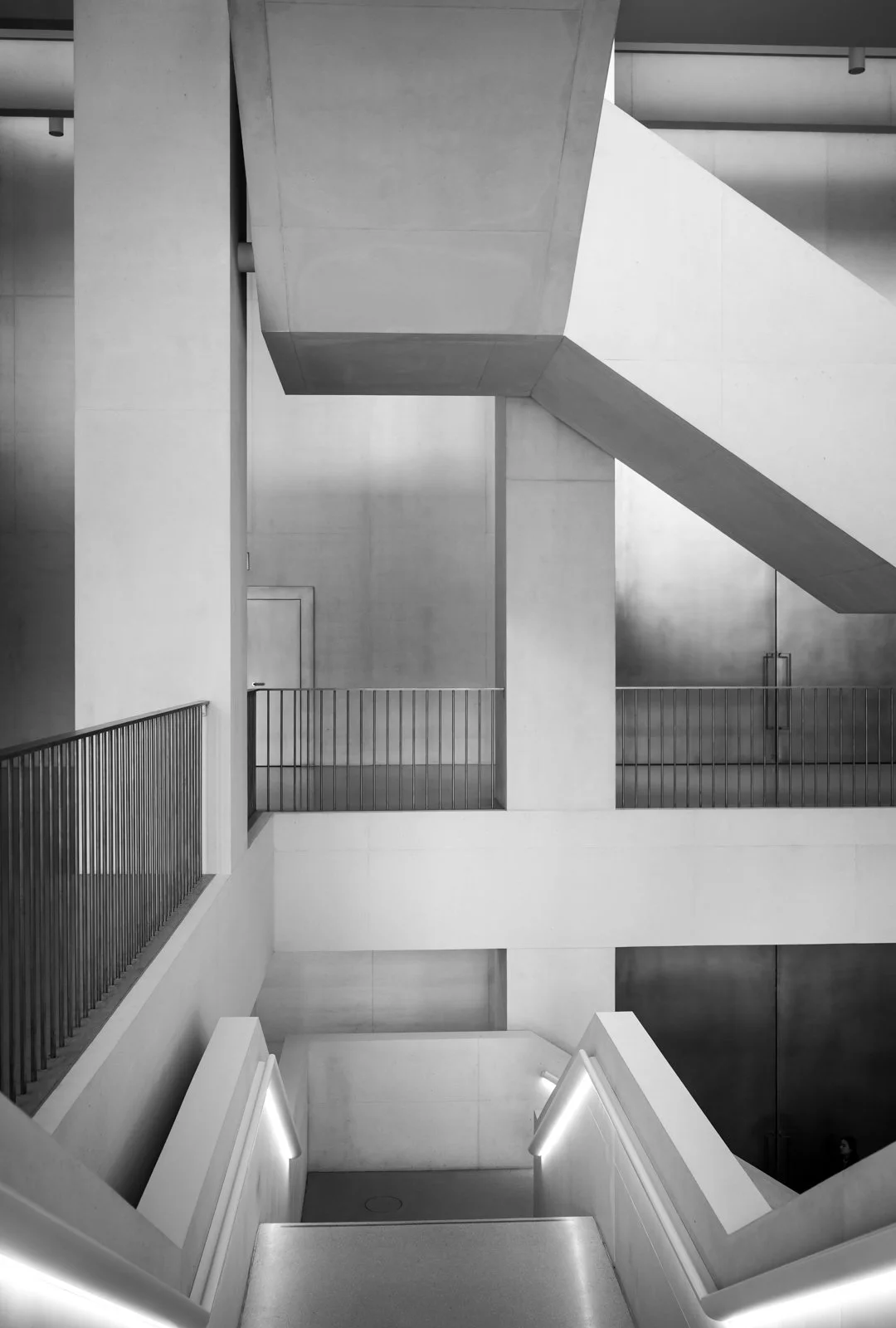 Schwarz-weiße Aufnahme eines modernen, geometrischen Treppenhauses mit geraden Linien und Lichtakzenten.
