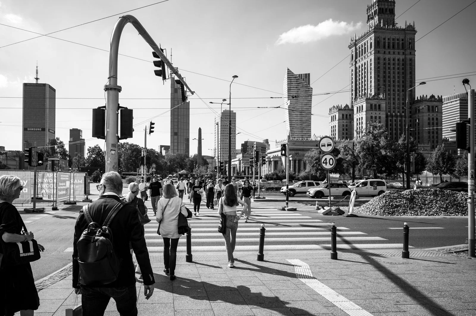 Menschen gehen an einer Kreuzung mit Hochhäusern im Hintergrund in einer Stadt vorbei.