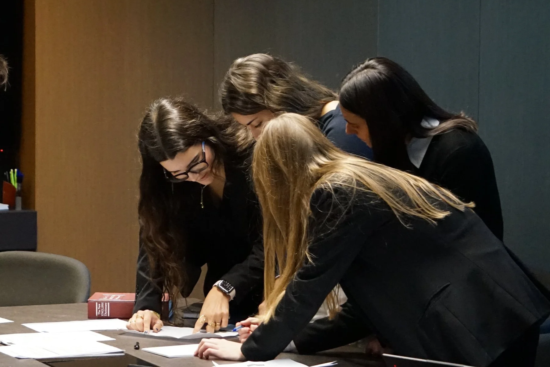 Cinco mujeres en la mesa, revisando papeles, en una reunión o trabajo en grupo.