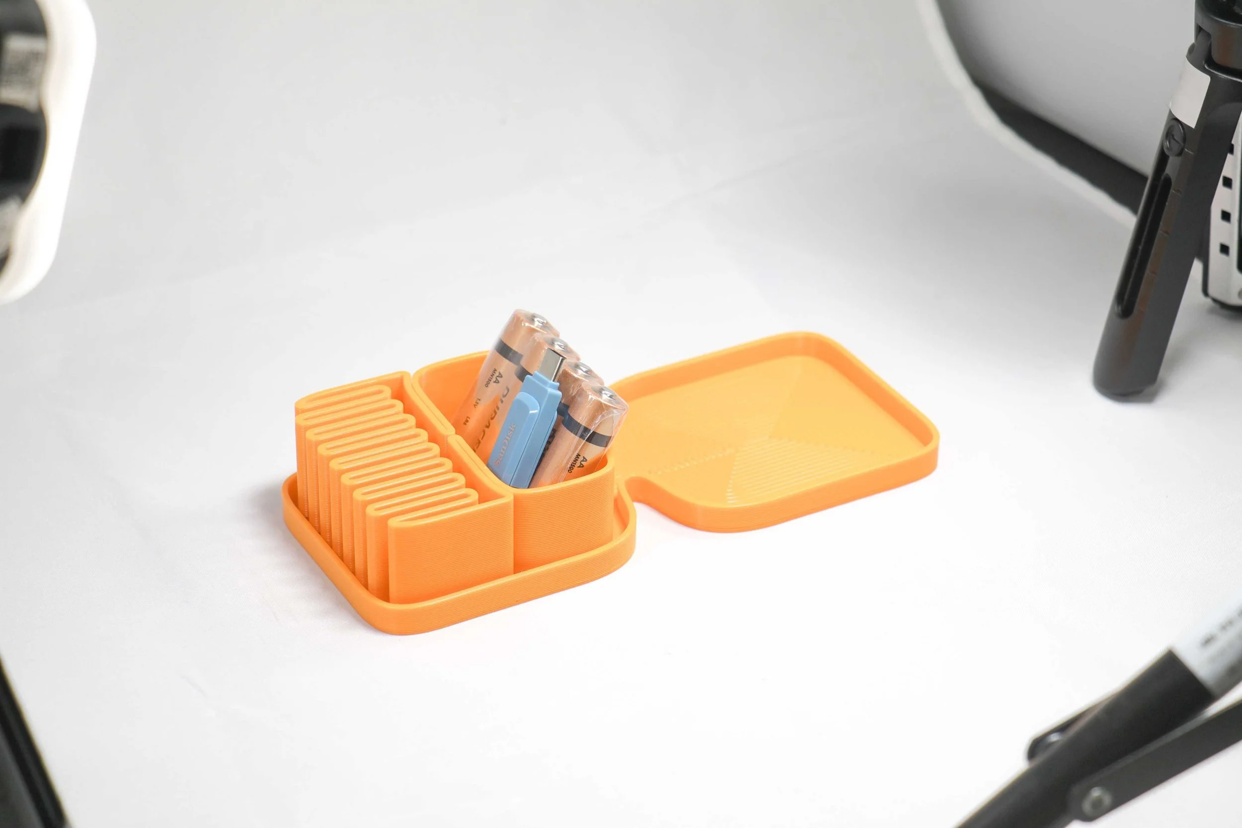 Orange storage container with multiple AA batteries stored upright, some with visible markings, placed on a white surface.
