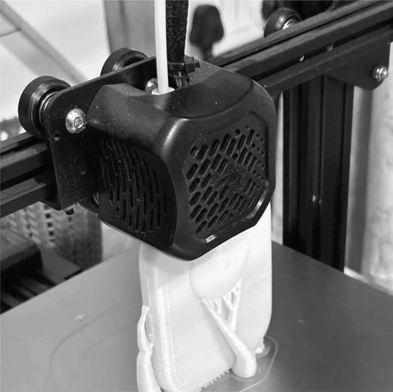 3D printer extruding white filament to create a plastic object on a printing bed.