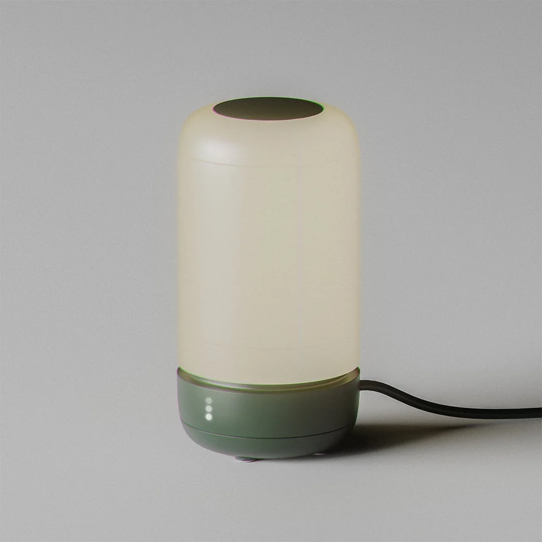 A modern, cylindrical table lamp with a soft white glow, sitting on a gray surface with a black power cord extending to the right.