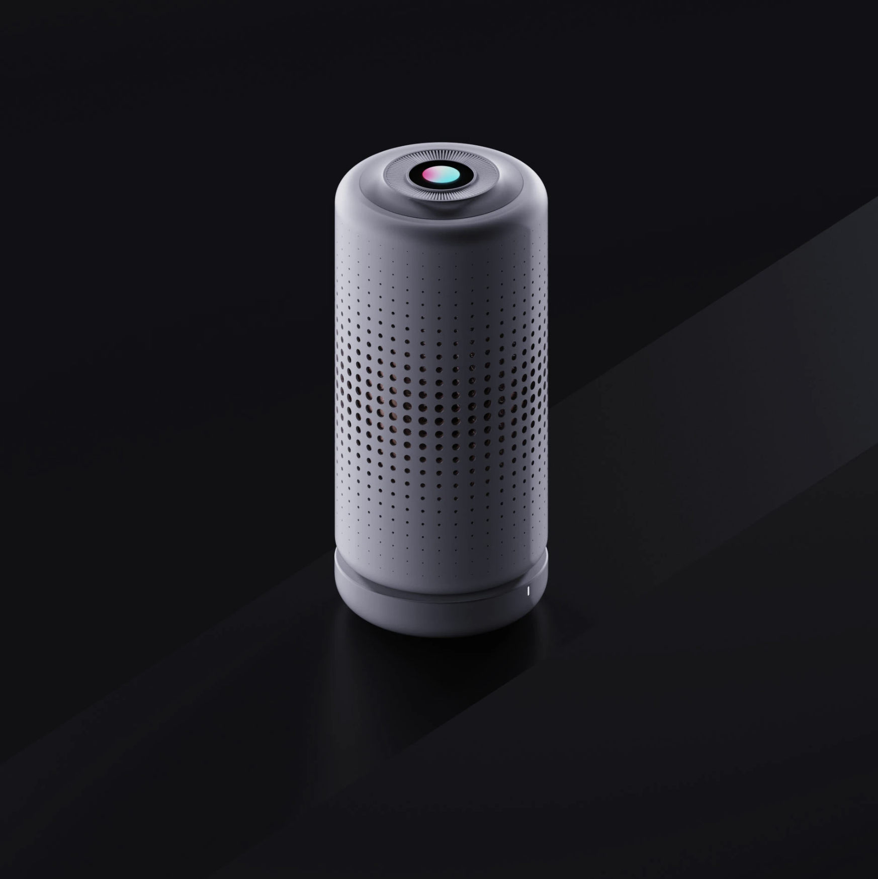 A white, cylindrical smart speaker with a perforated surface and a colorful circular touchpad on top, set against a dark background.