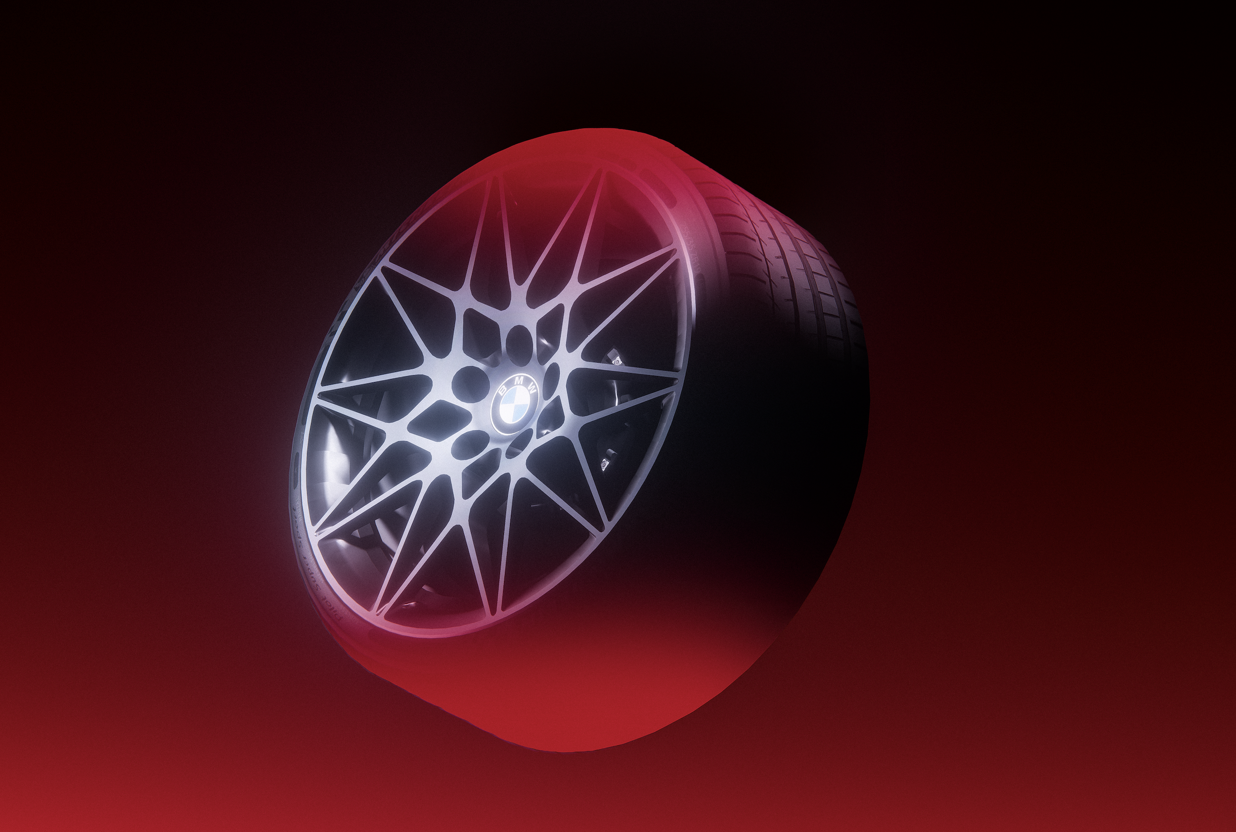 A BMW wheel with a geometric design on a black background, illuminated with white and red lighting.