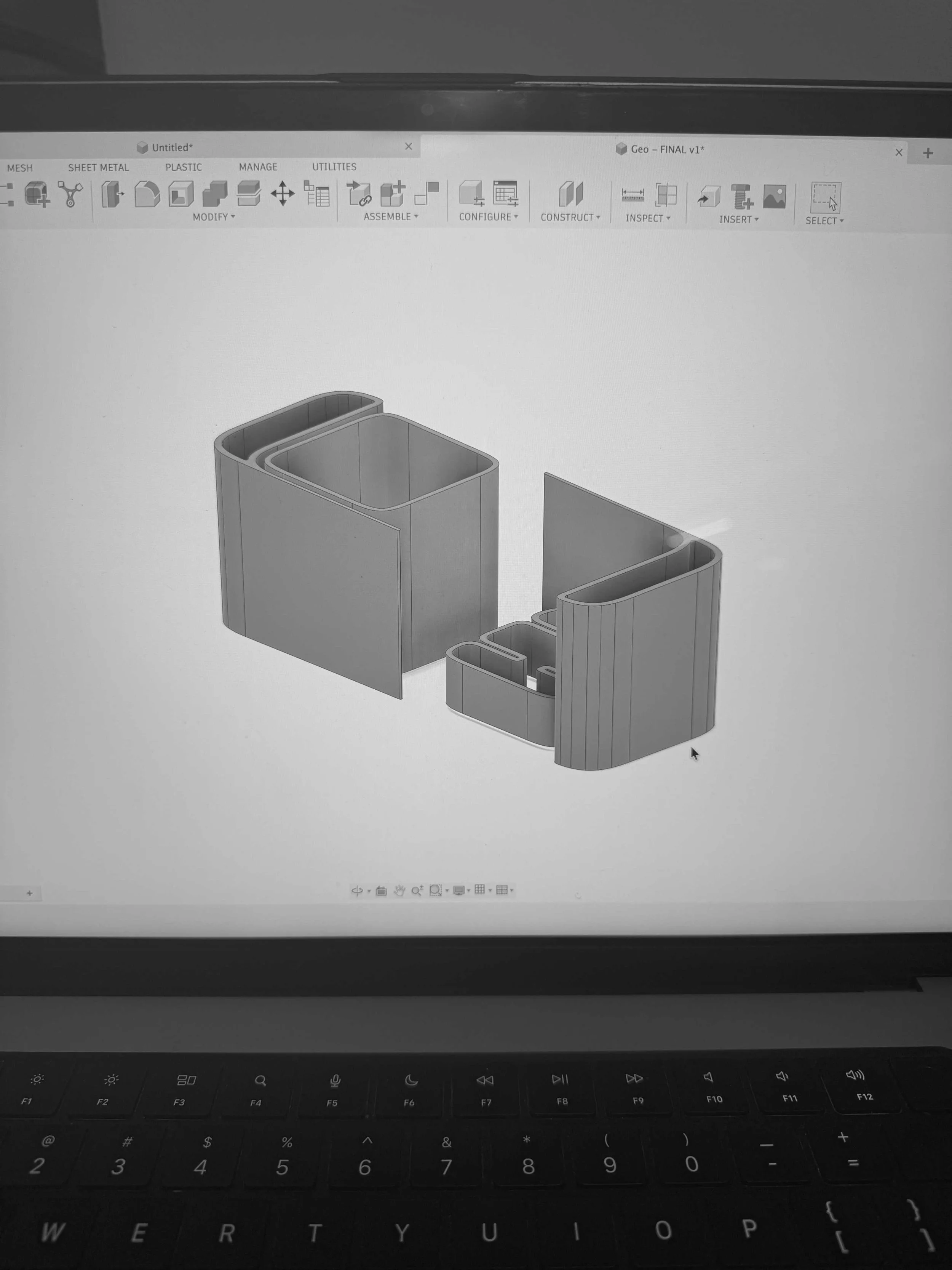 A computer screen displaying a 3D design of two rectangular containers or structures on CAD software with a black keyboard below.