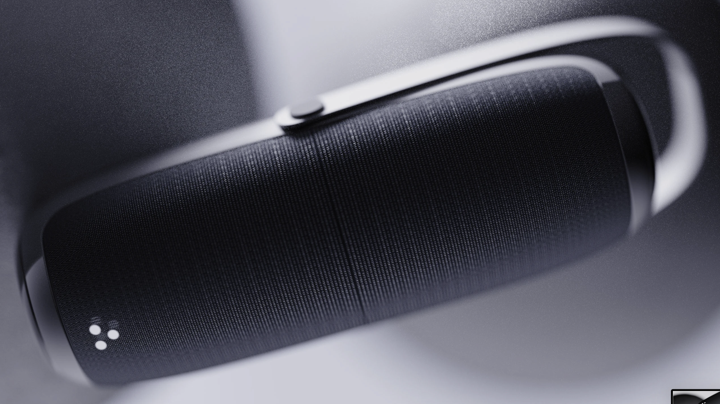 Close-up of a portable Bluetooth speaker with a textured black grille and a button on the top, placed on a light surface.