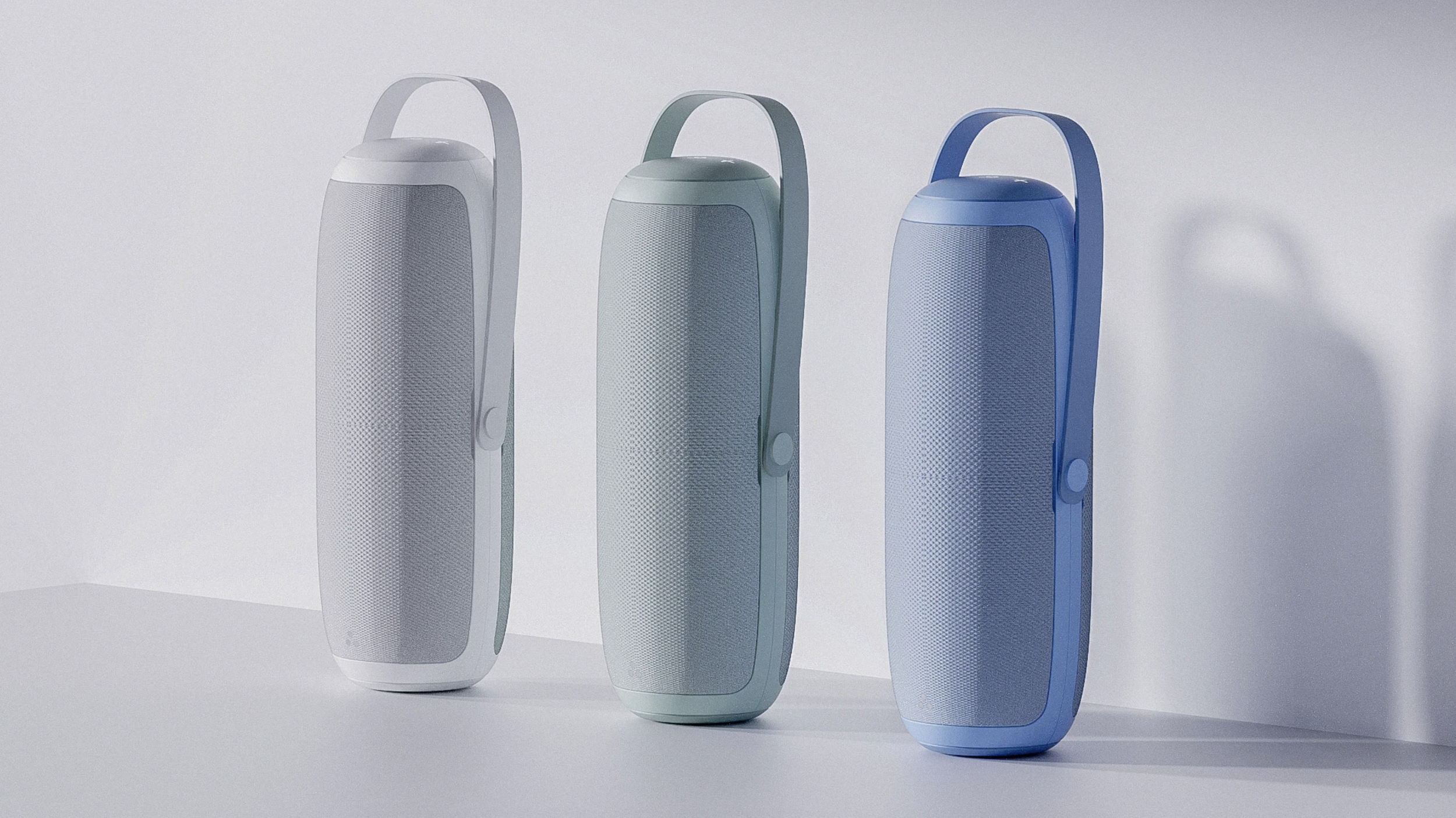 Three portable Bluetooth speakers in white, mint green, and blue, standing upright on a white surface against a light background.