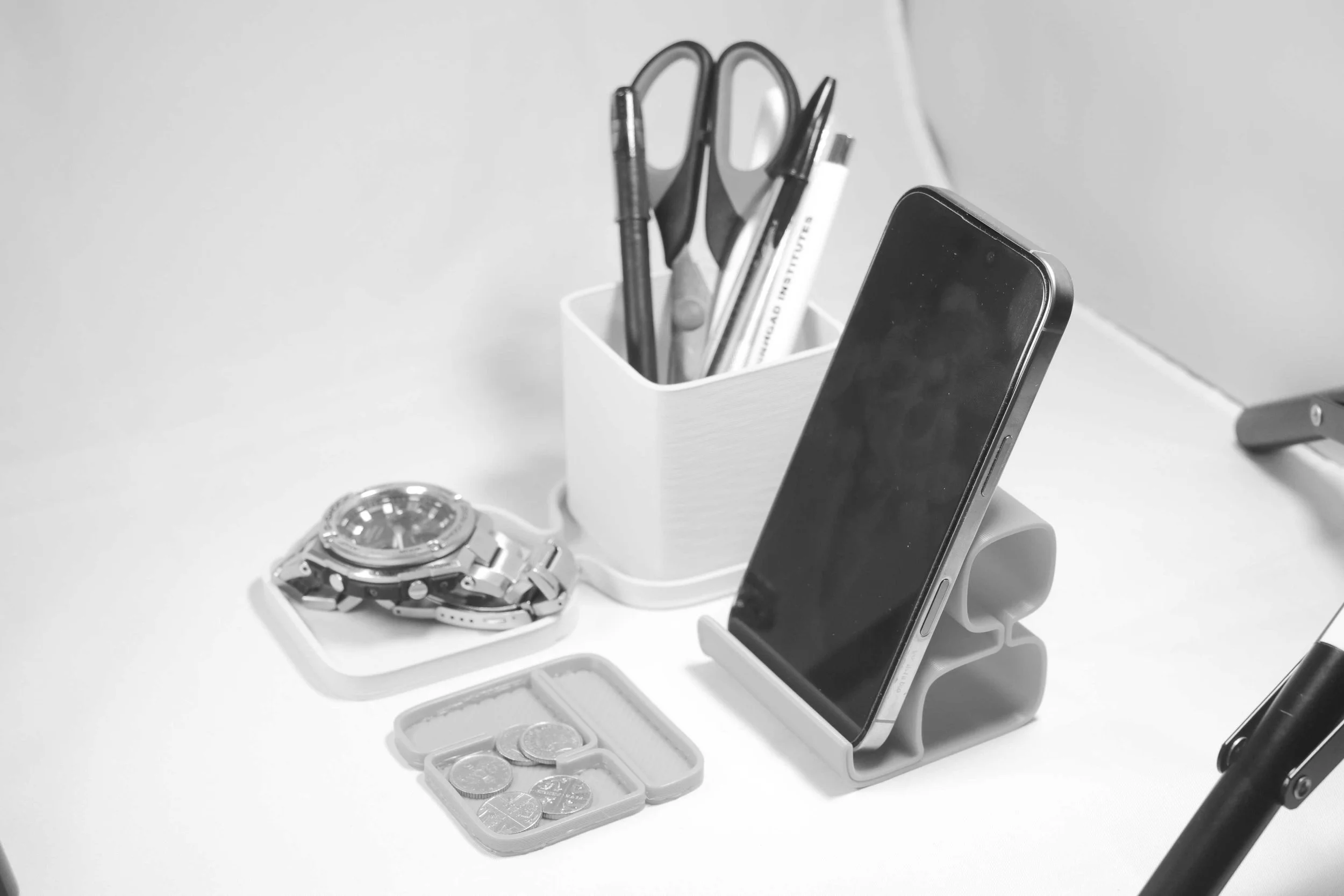 Desk with a wristwatch, coins, a smartphone in a stand, a pen holder with scissors and pens.