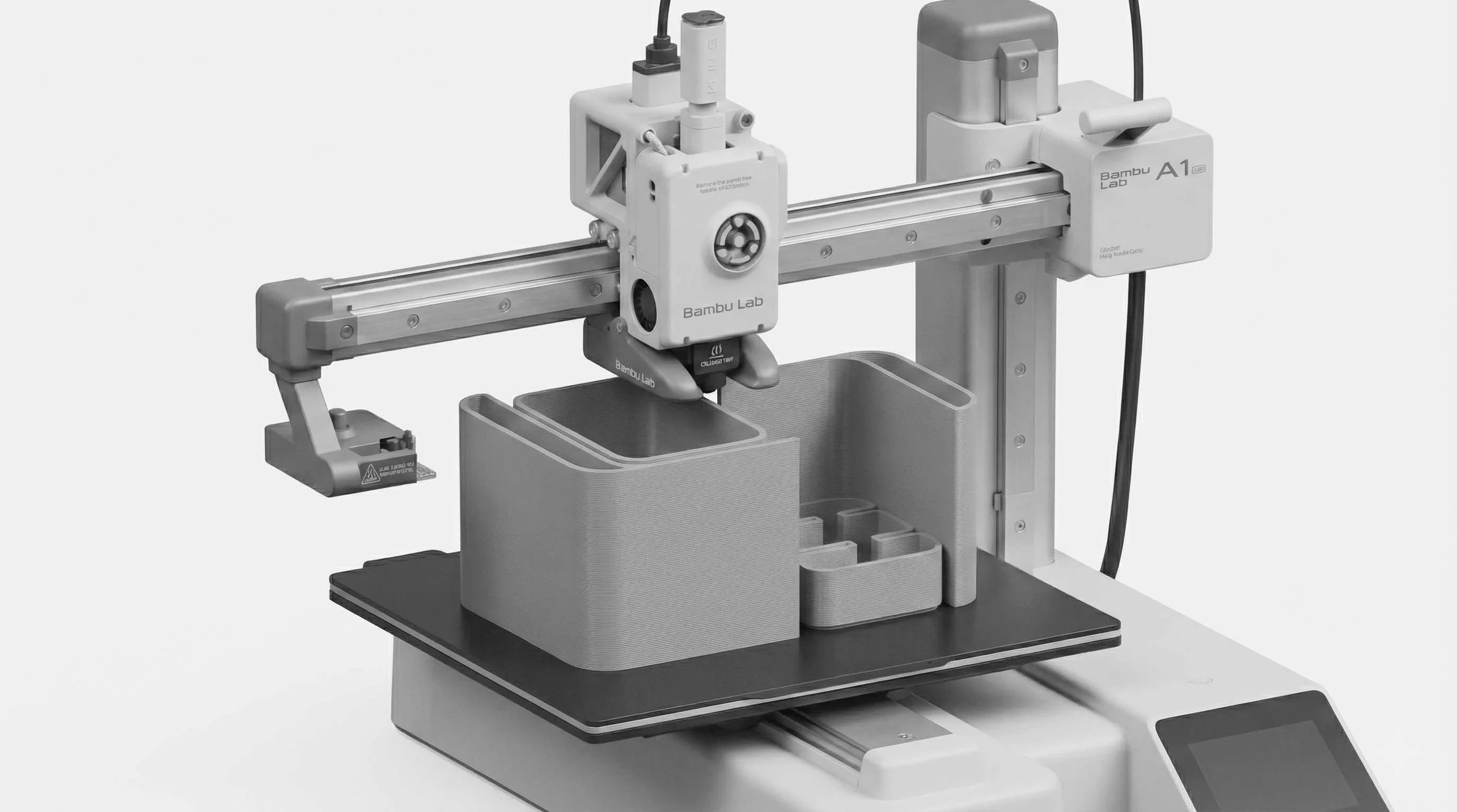 A 3D printer with a printing bed, printing a gray object with compartments and structures.