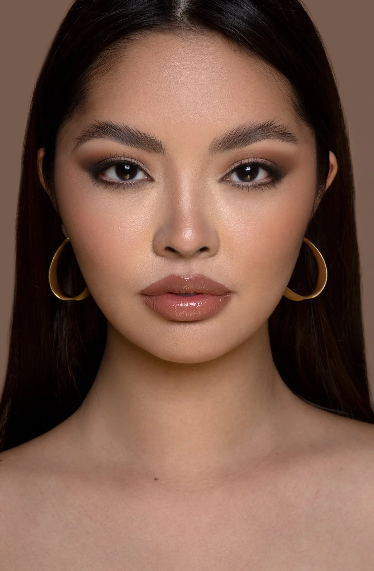 Close-up portrait of a woman with long dark hair, hoop earrings, and makeup with neutral tones.