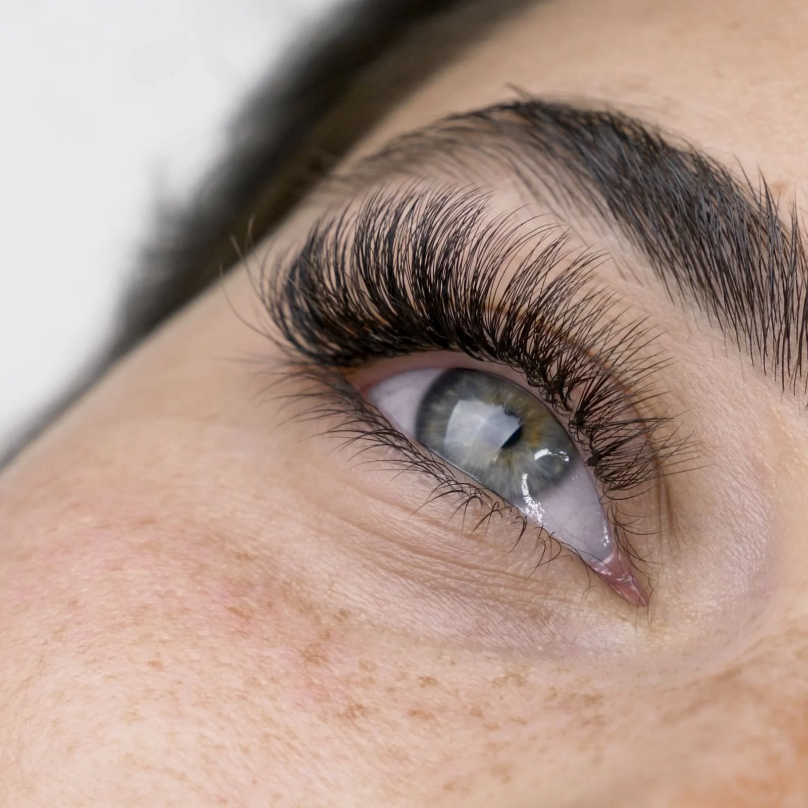 Close-up of a person's eye with long, thick eyelashes and gray-green iris.