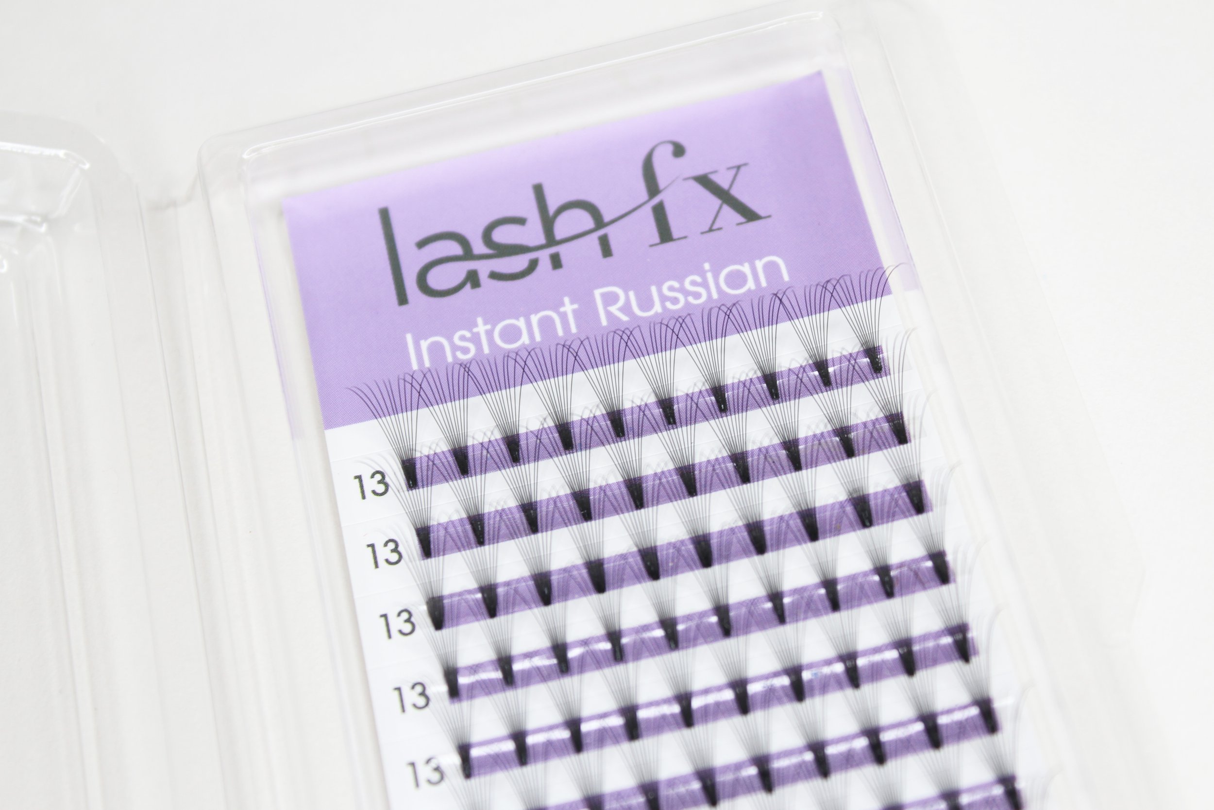 Close-up of a package of Lash Fix Instant Russian eyelash extensions with individual black false eyelashes arranged in rows on a purple and white background.