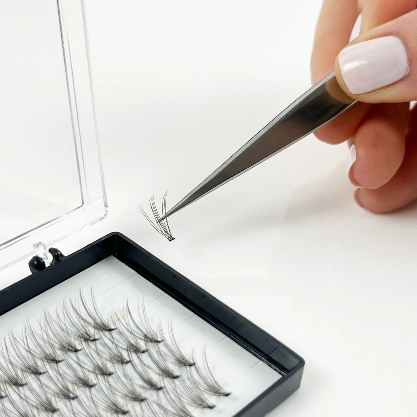 A hand holding tweezers placing individual false eyelashes into a storage tray with multiple false eyelashes arranged in rows.