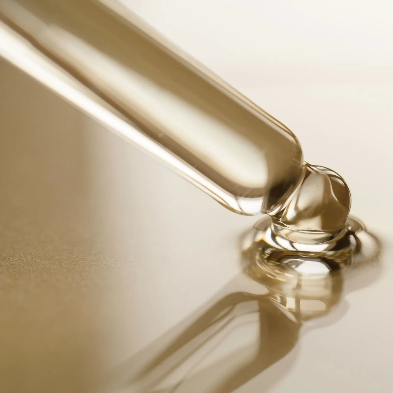 Close-up of a glass dropper releasing a clear liquid onto a reflective surface.