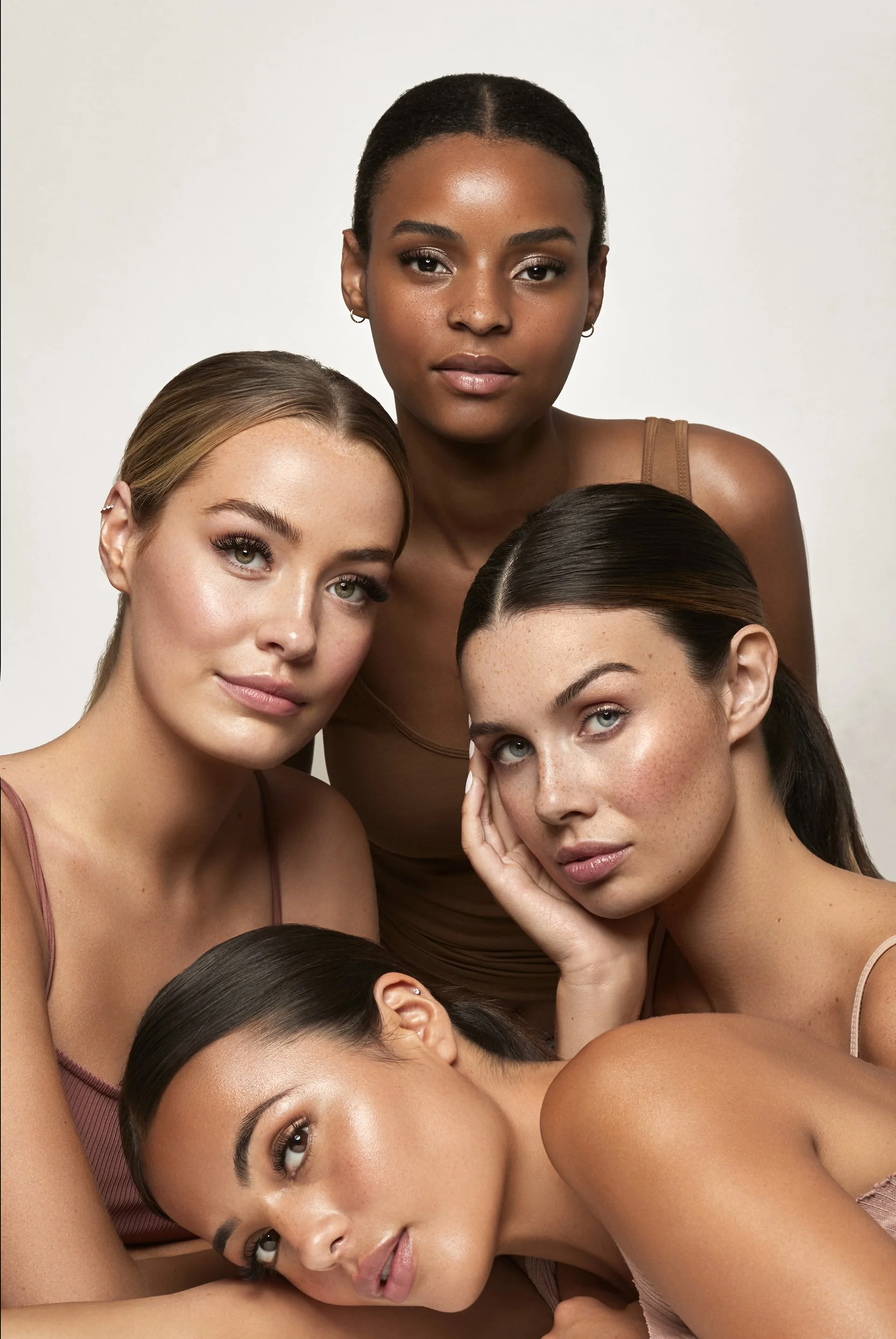 Five women with diverse skin tones and hair colors posing together in a close-up portrait against a plain light background.