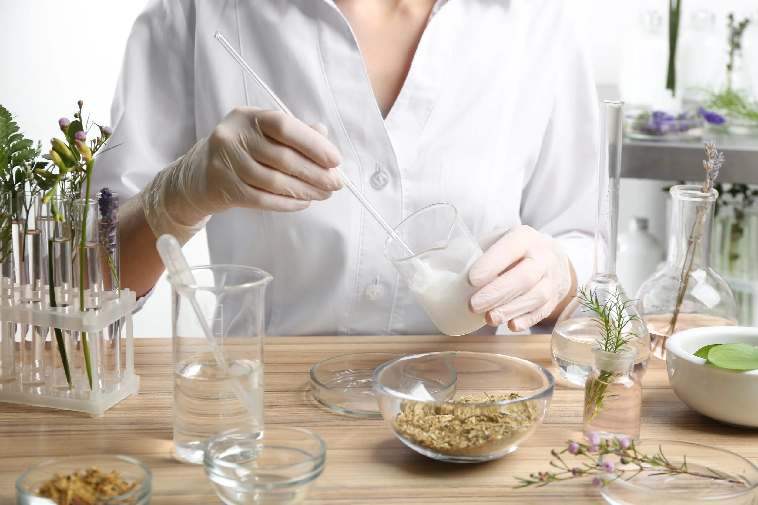 Scientist in a white lab coat and gloves conducting a scientific experiment with various glassware and plants.