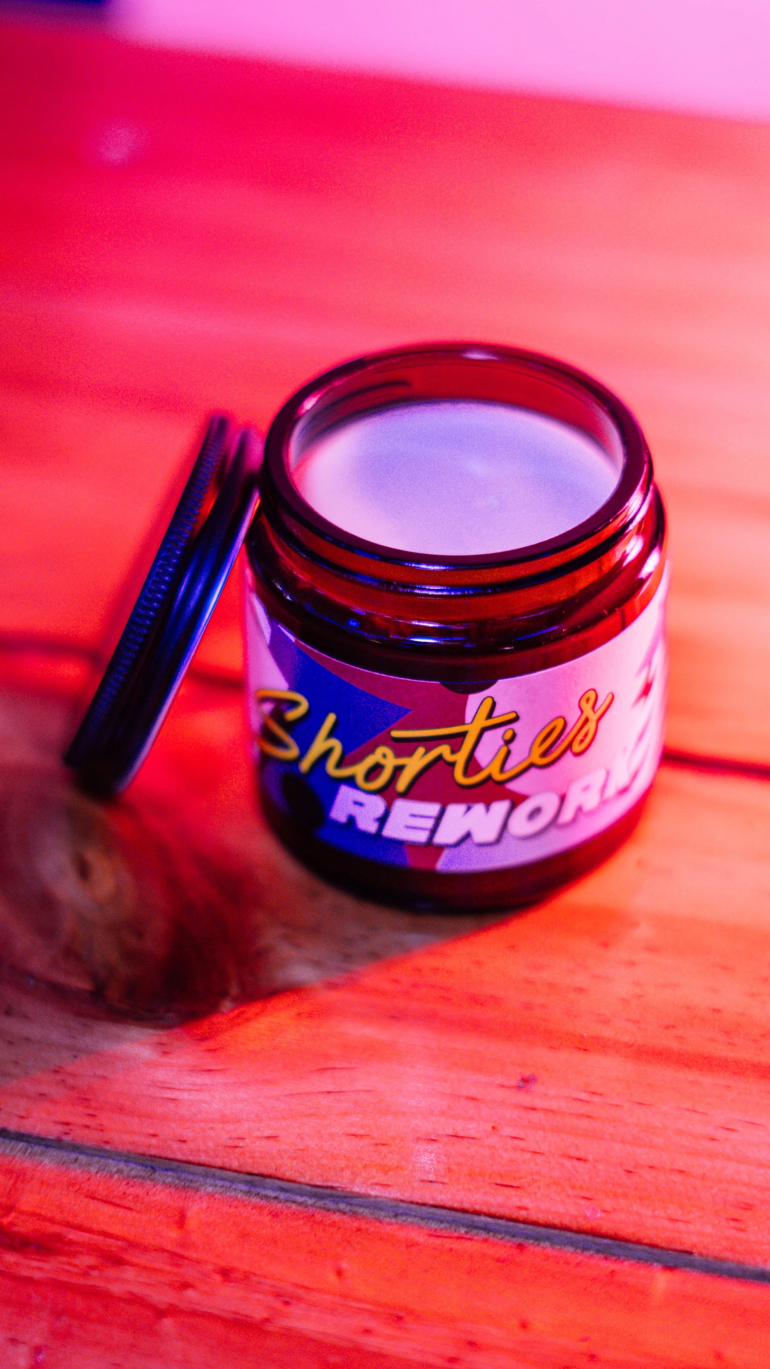 An open jar labeled 'Shorties REWORK' sitting on a wooden surface with a slightly blurred background.