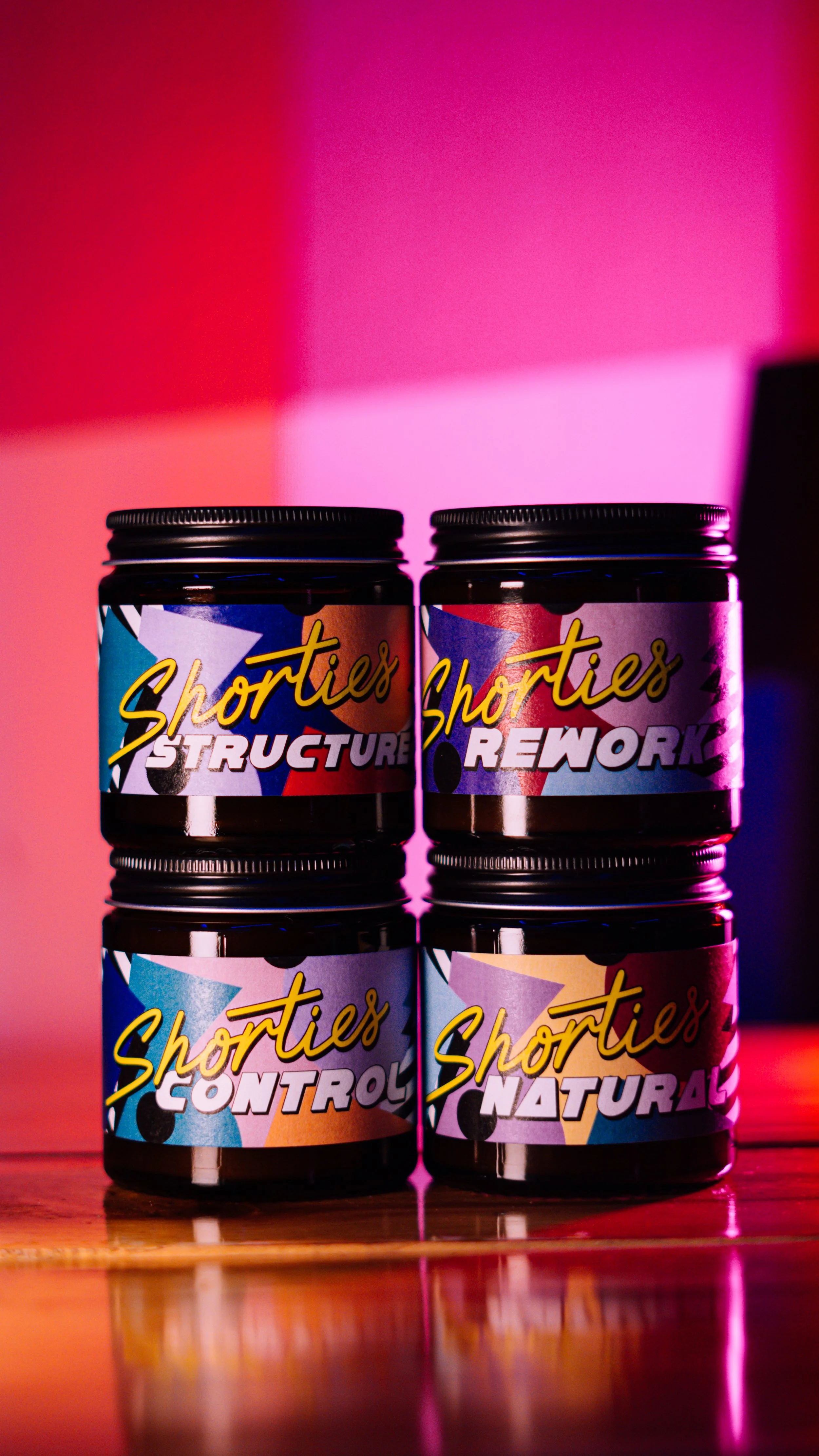 Four jars labeled 'Shorties' with different variants: Structure, Rework, Control, Natural, stacked two by two on a wooden surface with colorful background lighting.