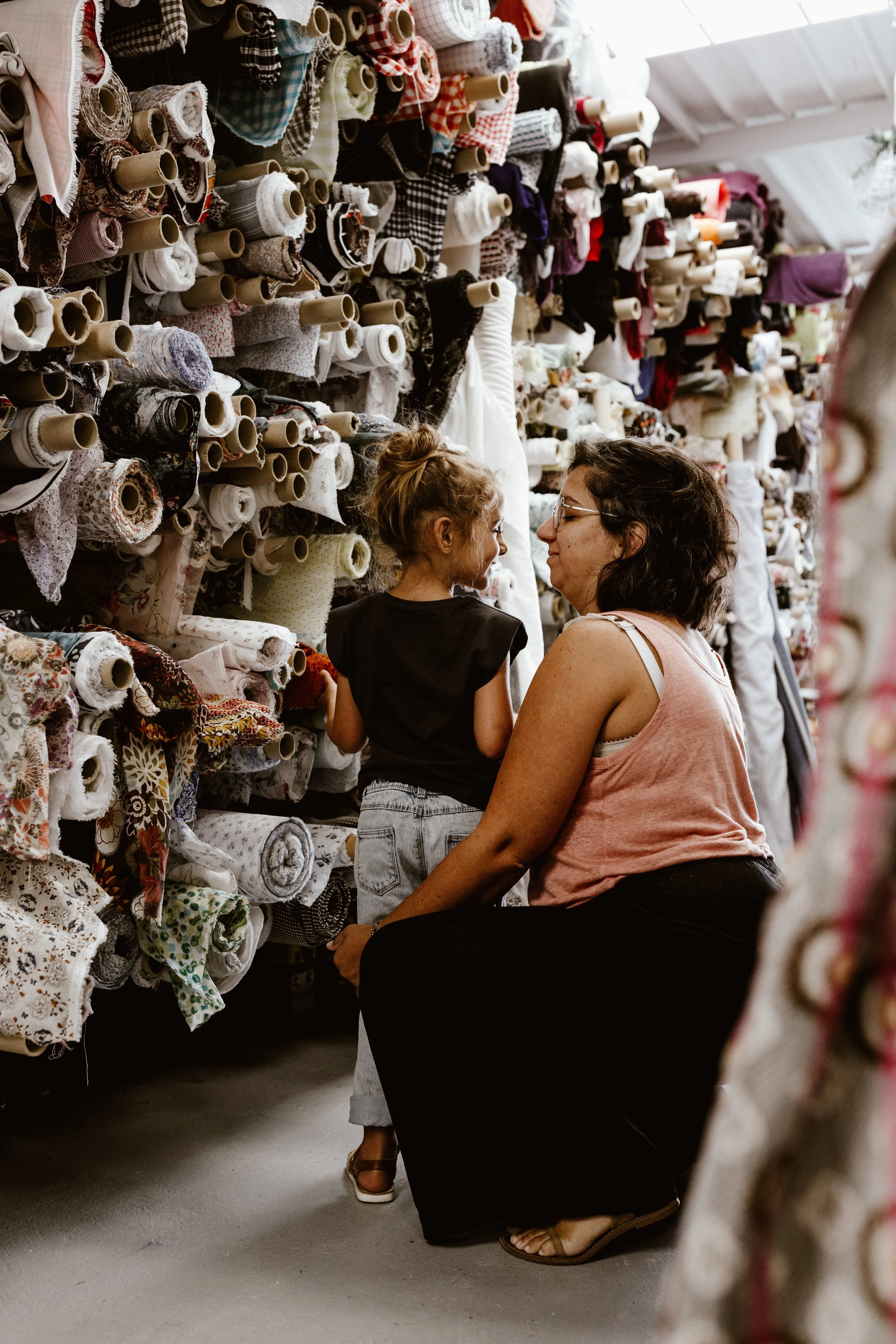 Une femme et une petite fille regardant des rouleaux de tissu dans une boutique de tissus.
