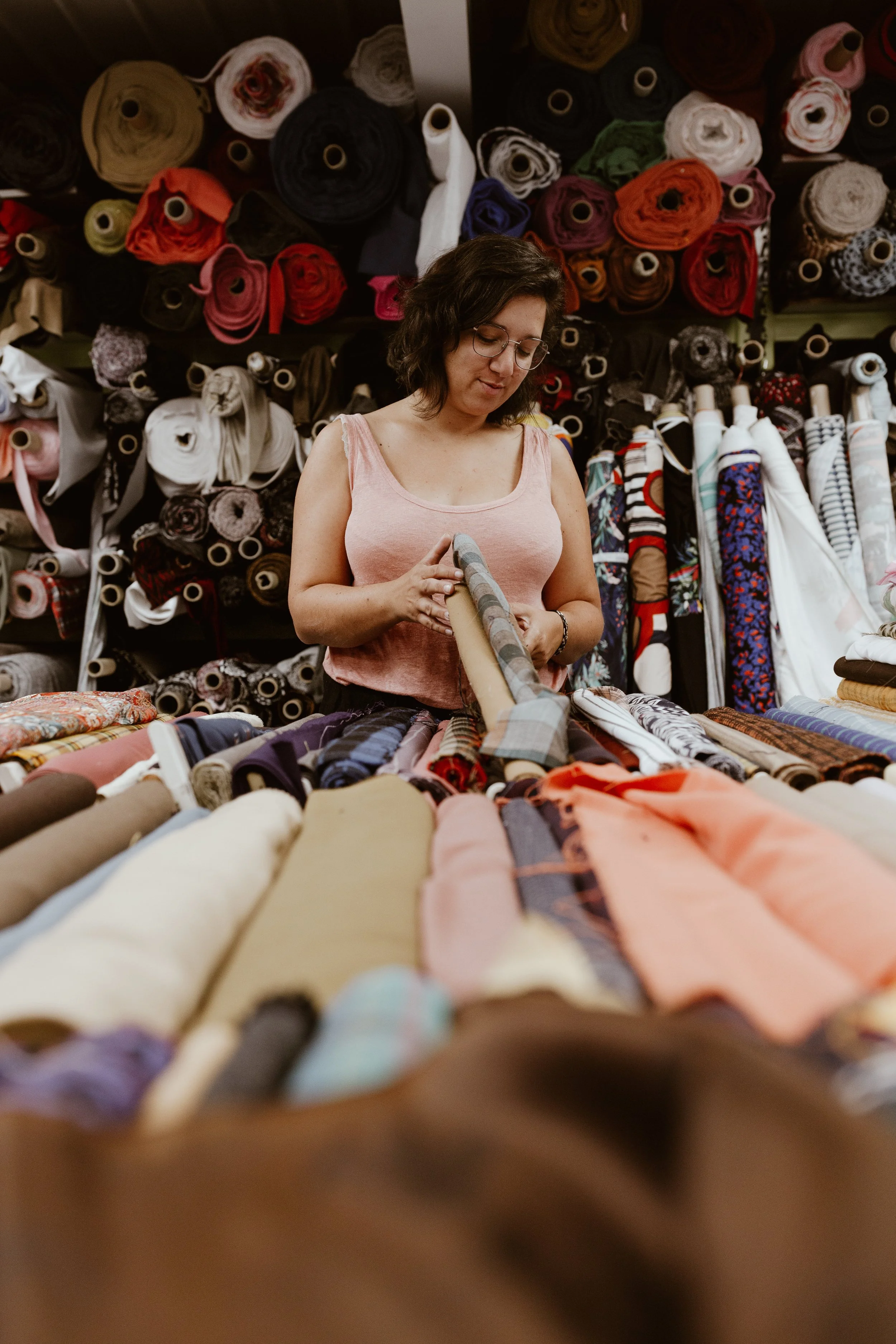 Une femme dans une boutique de tissus, entourée de rouleaux de tissu de différentes couleurs et motifs.
