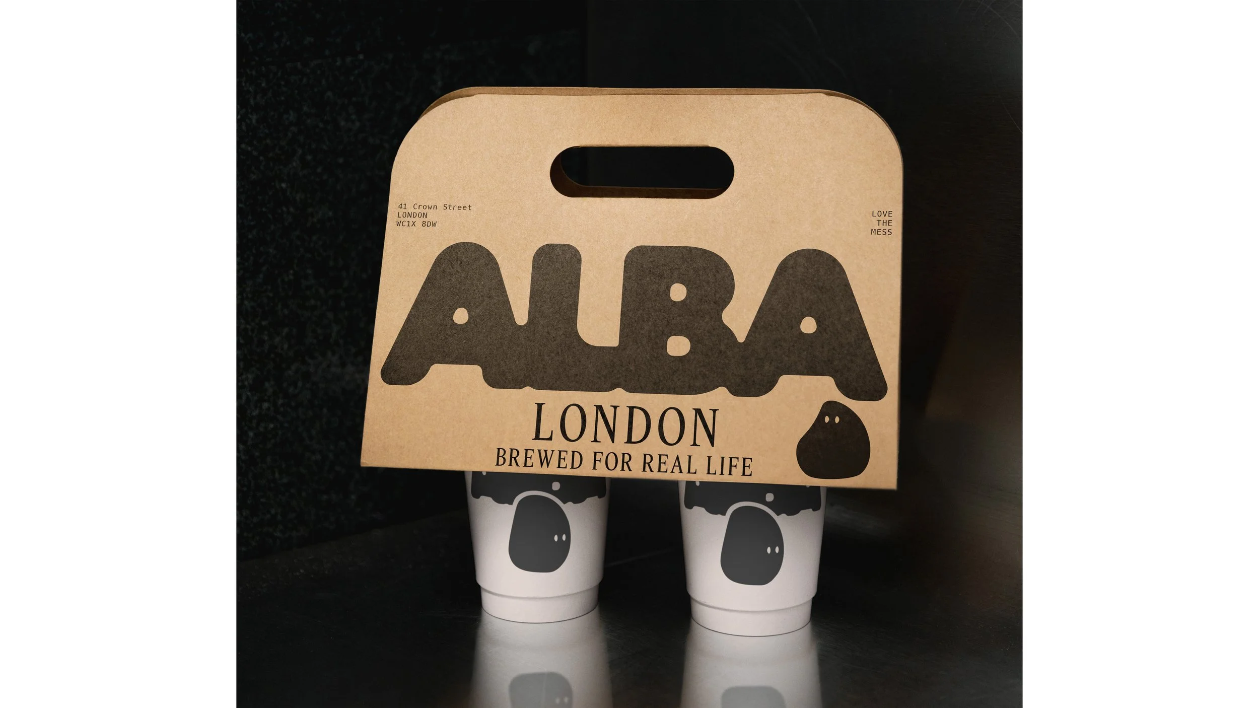 Two white beverage cups with black and white dog face illustrations, placed under a brown cardboard carrying case with text and graphics, on a black surface.